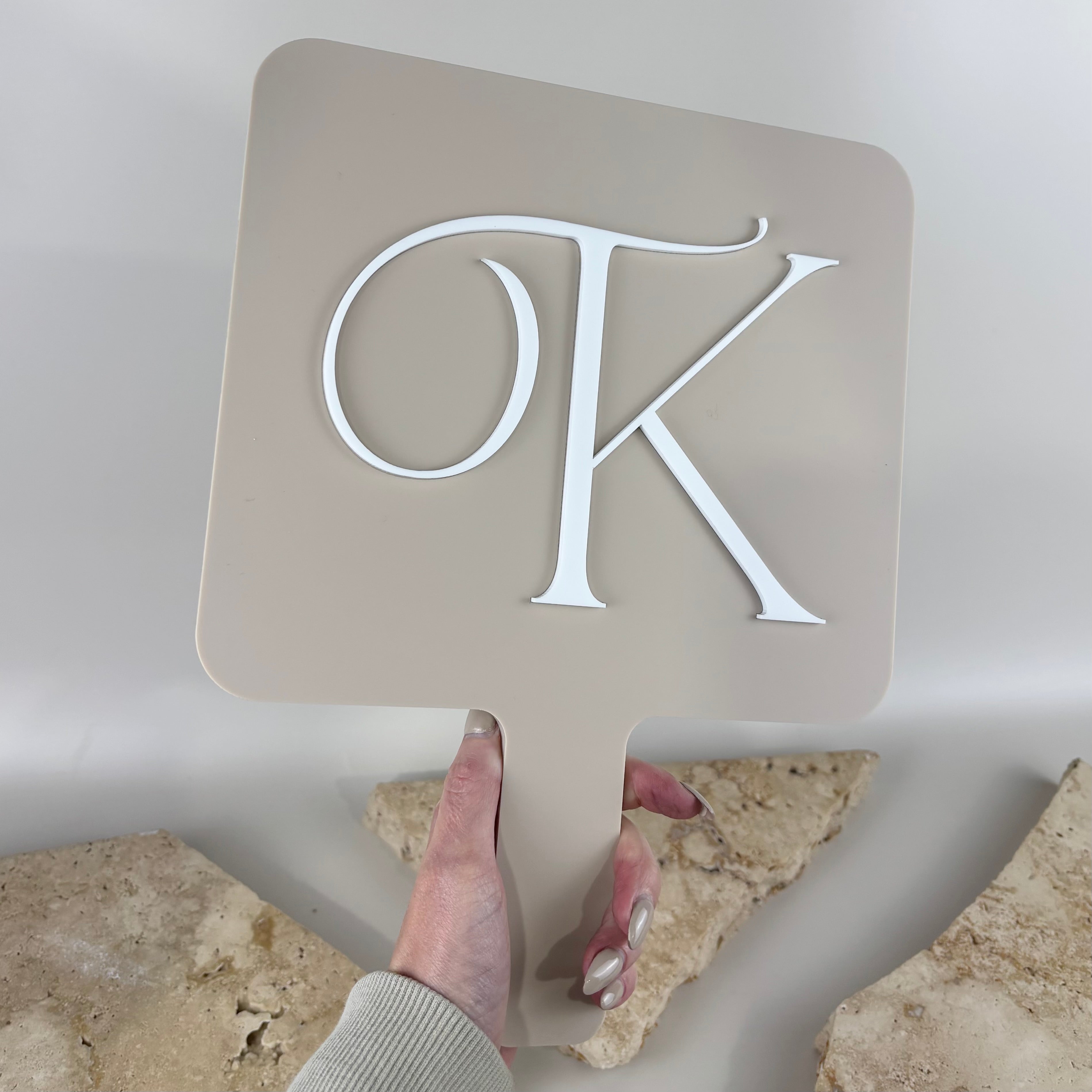 Custom handheld acrylic salon mirror in a neutral beige finish featuring raised 3D white acrylic initials. Personalised beauty mirror with ergonomic handle, ideal for hair salons, nail salons, lash artists, makeup artists and beauty professionals for client reveals, branding and social media photos.