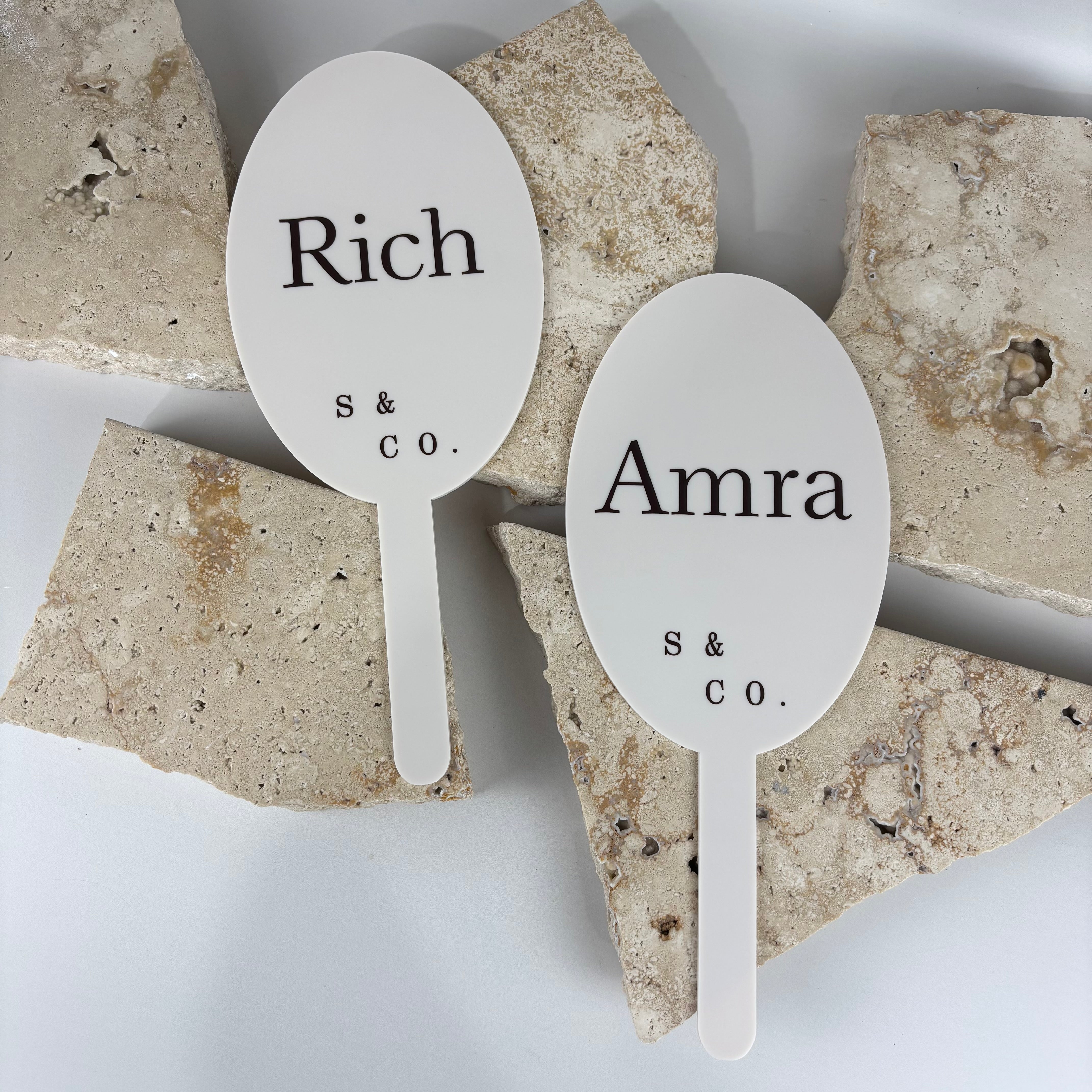 Custom acrylic brand paddles in matte white with black lettering, personalised with business names Rich S & Co and Amra S & Co, designed for salon reveals, photos and client consultations.
