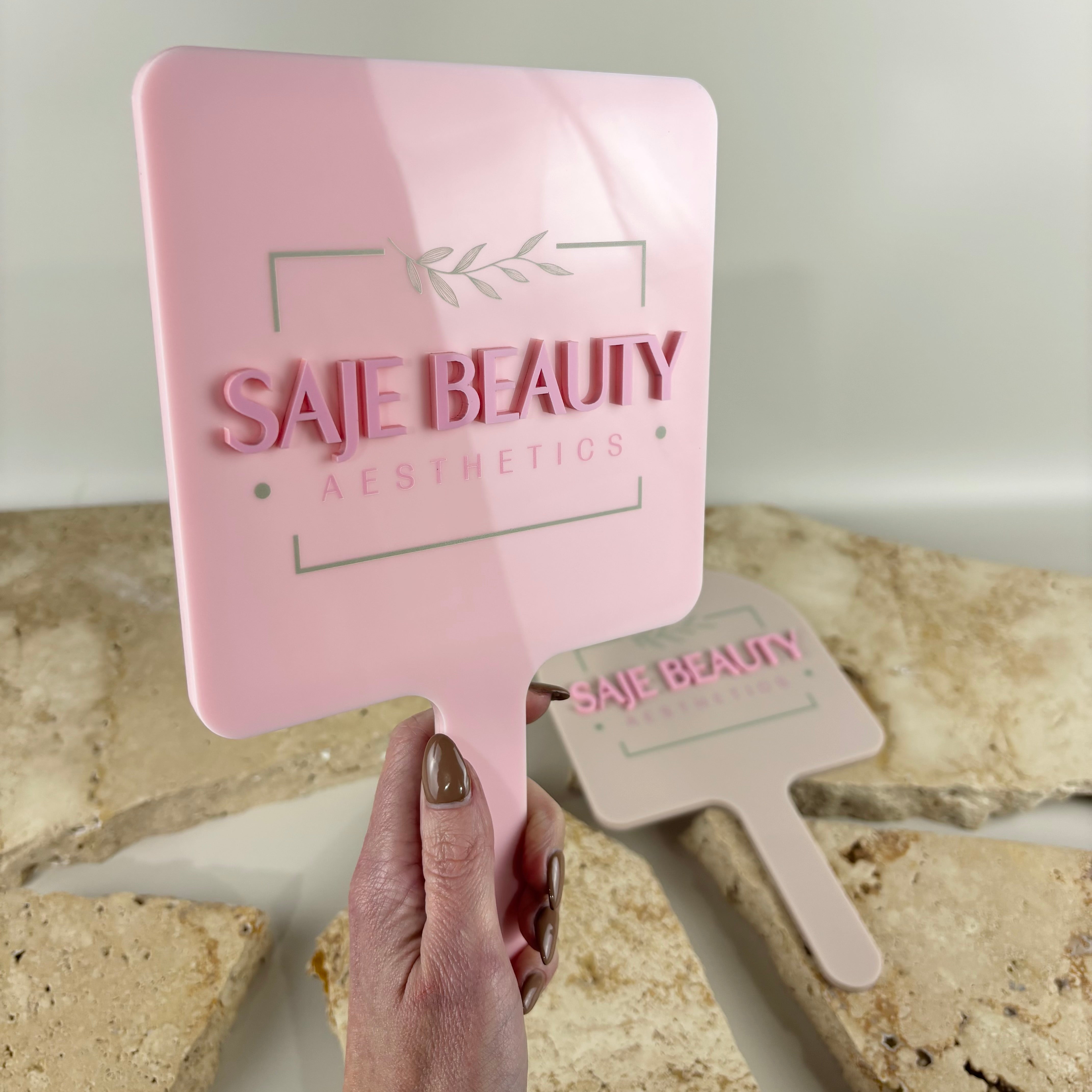 Luxury pink acrylic handheld mirror with raised 3D business logo for beauty salons and aesthetic clinics, personalised branded mirror for lash artists, makeup artists and skincare businesses in Australia and New Zealand.