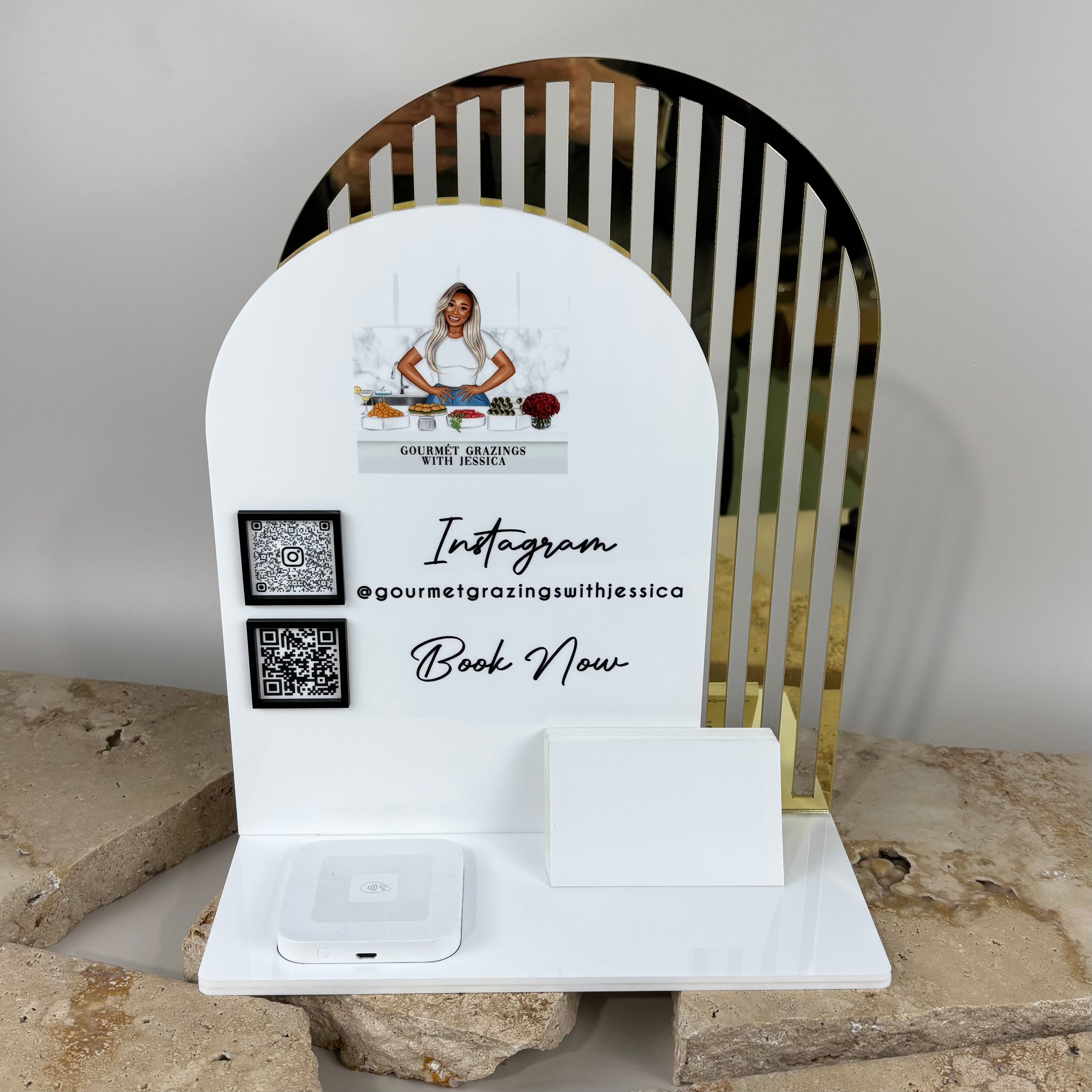 Custom acrylic NFC business station with arched white panel and gold mirror backing, featuring QR codes, Instagram handle and booking prompt, designed for small food and catering businesses to capture leads and social media follows.