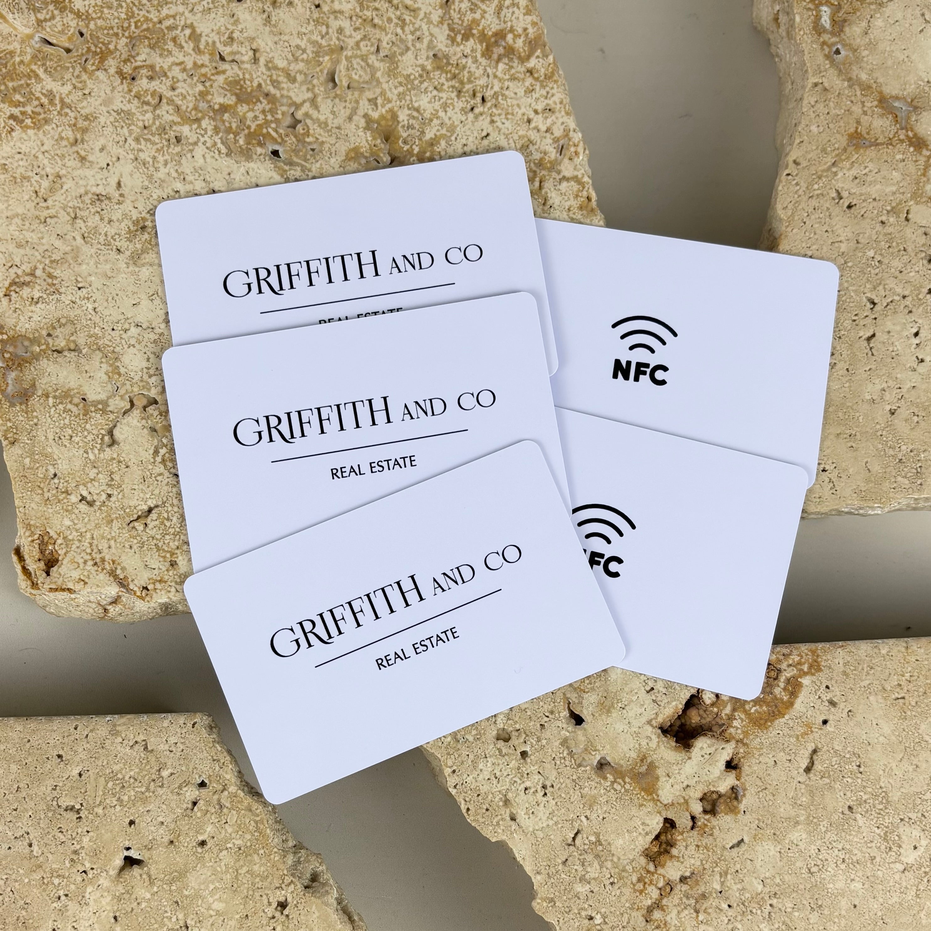 White NFC business cards for Griffith and Co Real Estate, featuring printed logo on the front and NFC tap icon on the back, displayed on natural stone for a clean, professional real estate branding aesthetic.