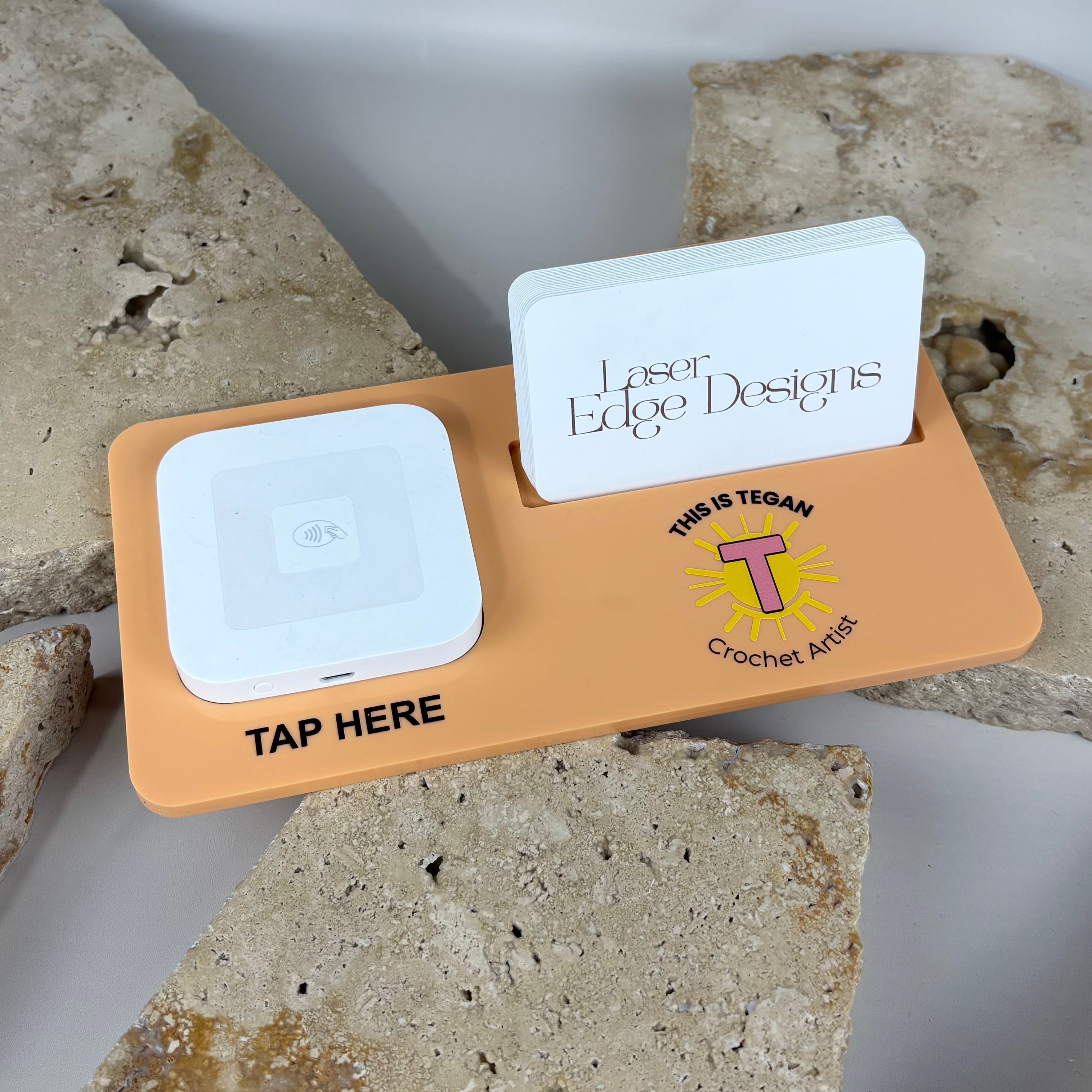 Peach acrylic NFC business card stand with built-in tap pad and card holder, branded for a small business, designed for contactless sharing at markets and counters, styled on a neutral stone background