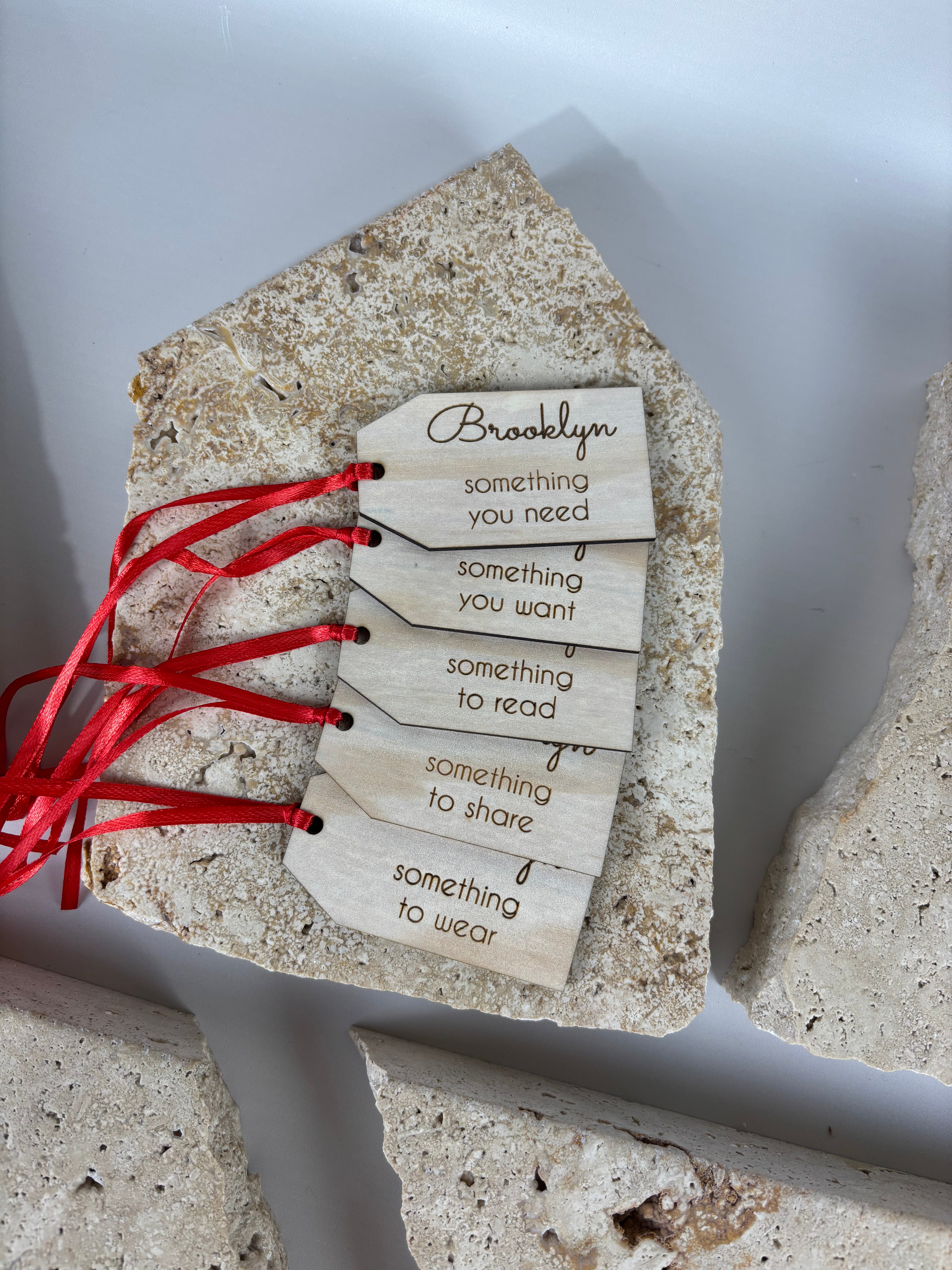 personalised wooden christmas gift tags with red ribbon displayed on stone background, engraved labels reading something you need something you want something to read something to share something to wear, custom name brooklyn on top tag, laser cut eco friendly christmas gifting tags australia made