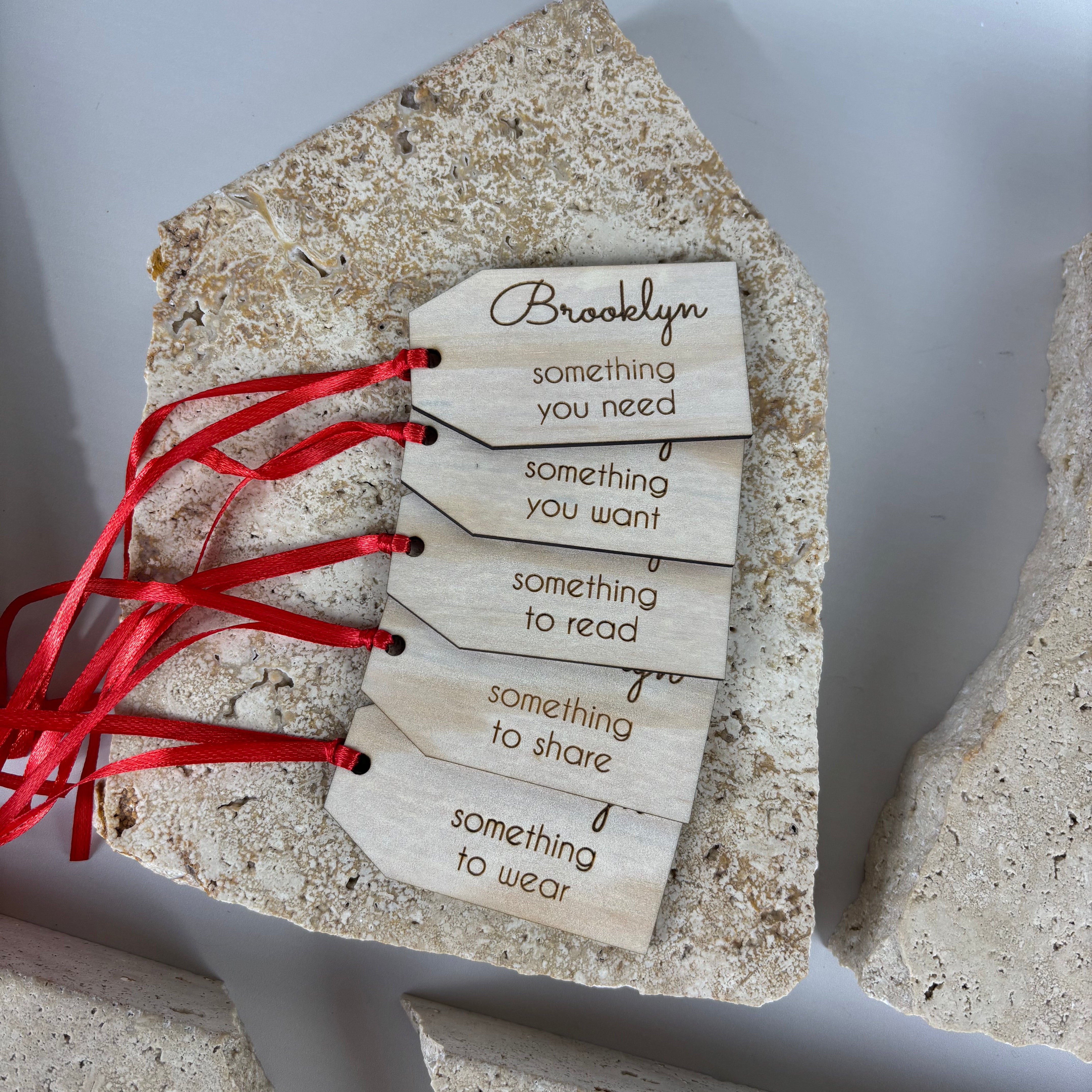 personalised wooden christmas gift tags with red ribbon displayed on stone background, engraved labels reading something you need something you want something to read something to share something to wear, custom name brooklyn on top tag, laser cut eco friendly christmas gifting tags australia made