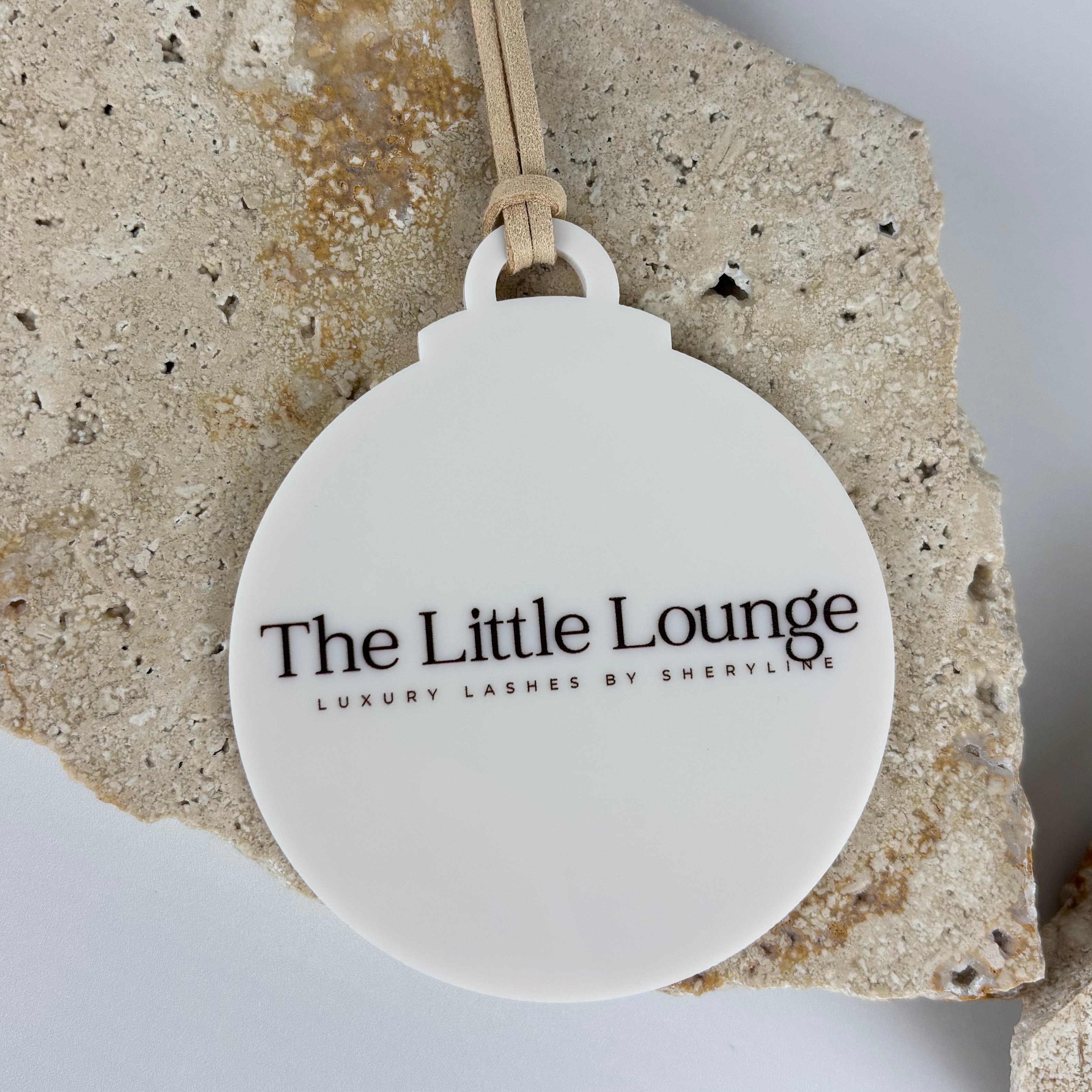 Custom UV printed acrylic branded bauble for The Little Lounge Luxury Lashes by Sheryline, featuring black logo text on matte white ornament with beige suede tie – Australian made by Laser Edge Designs.
