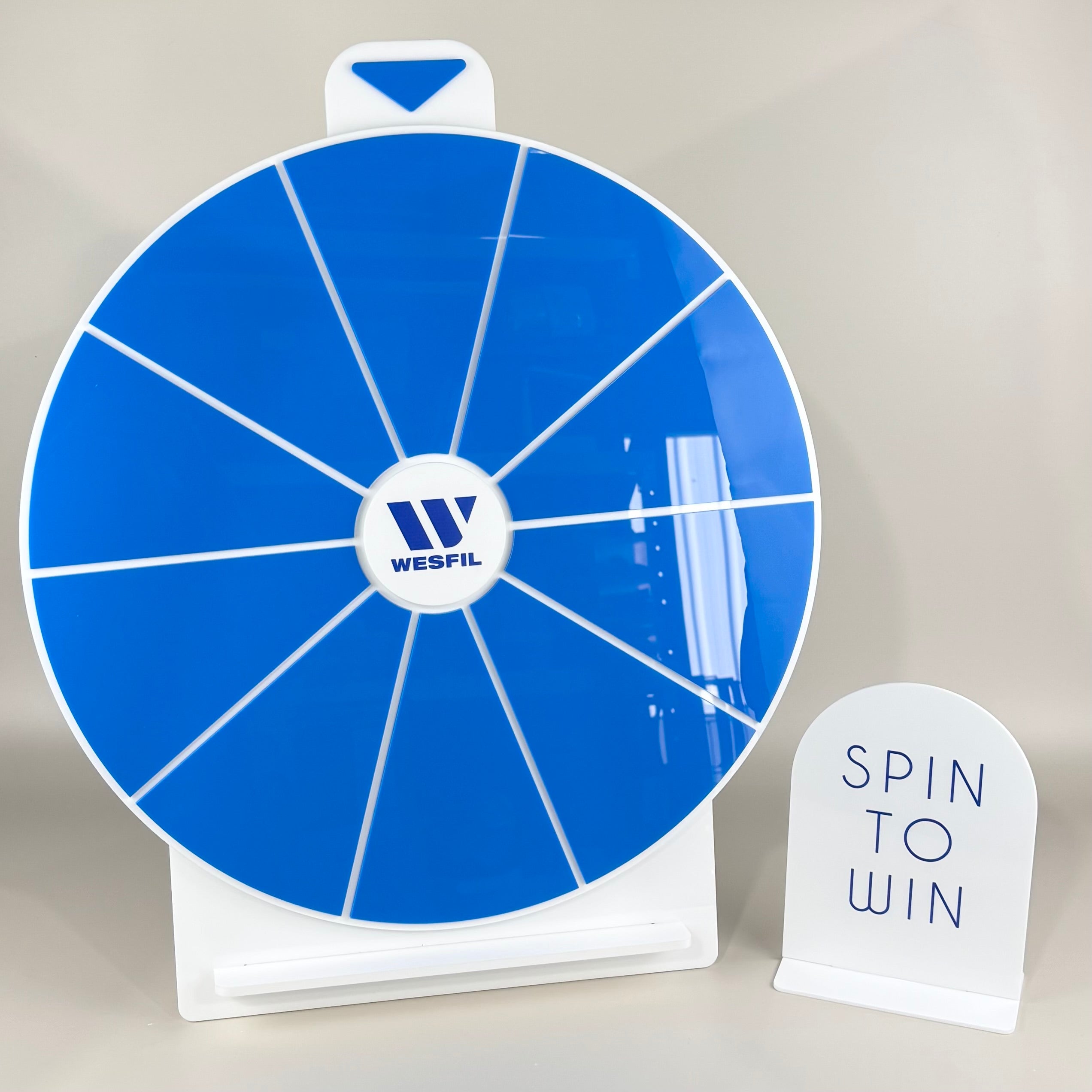 Custom blue acrylic spin to win prize wheel with Wesfil branded logo, blank giveaway sections ready for custom text, displayed with matching white acrylic “Spin to Win” counter sign, designed for trade shows, retail promotions and business marketing displays.