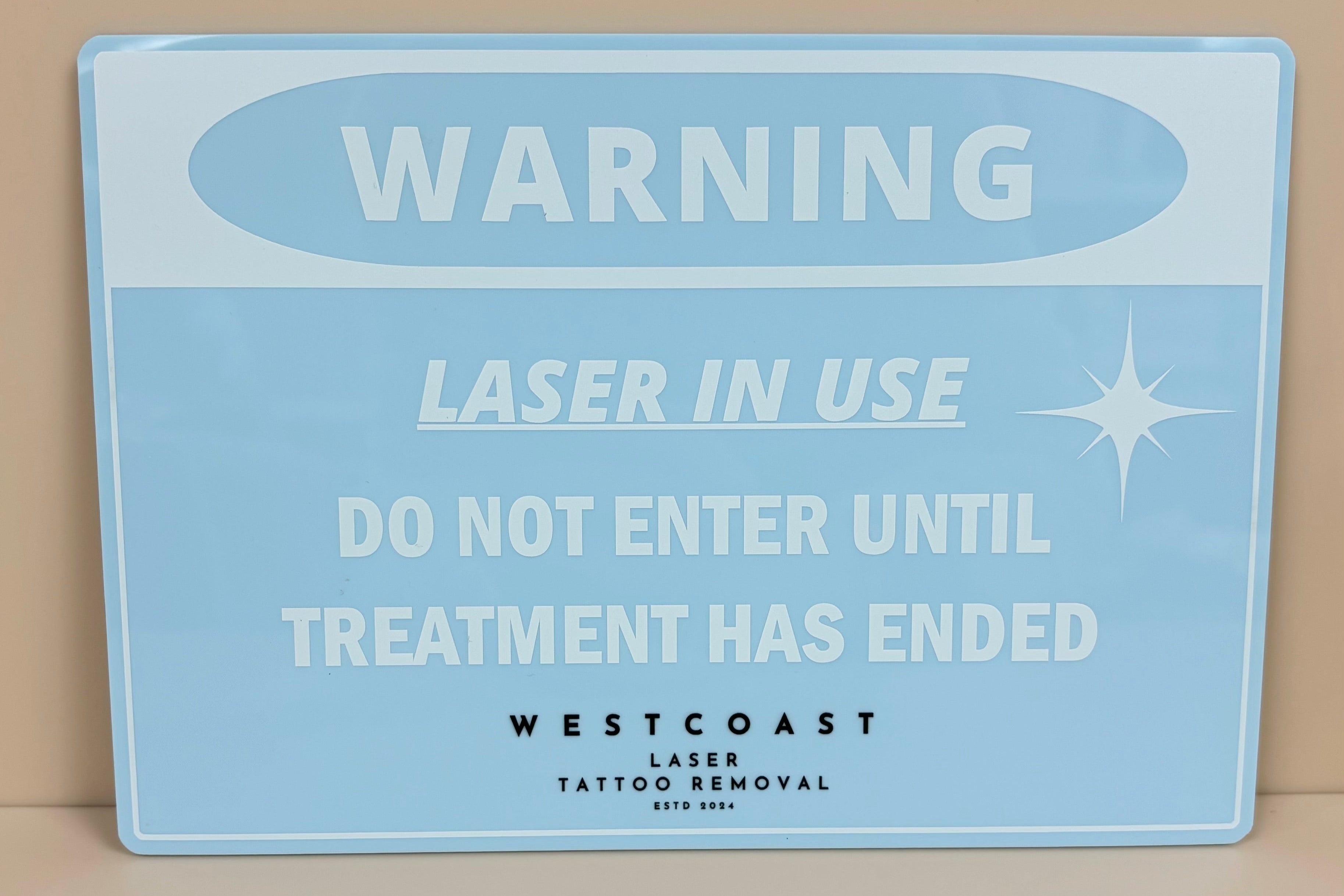 Blue acrylic laser in use sign with custom branding, mounted on treatment room wall.