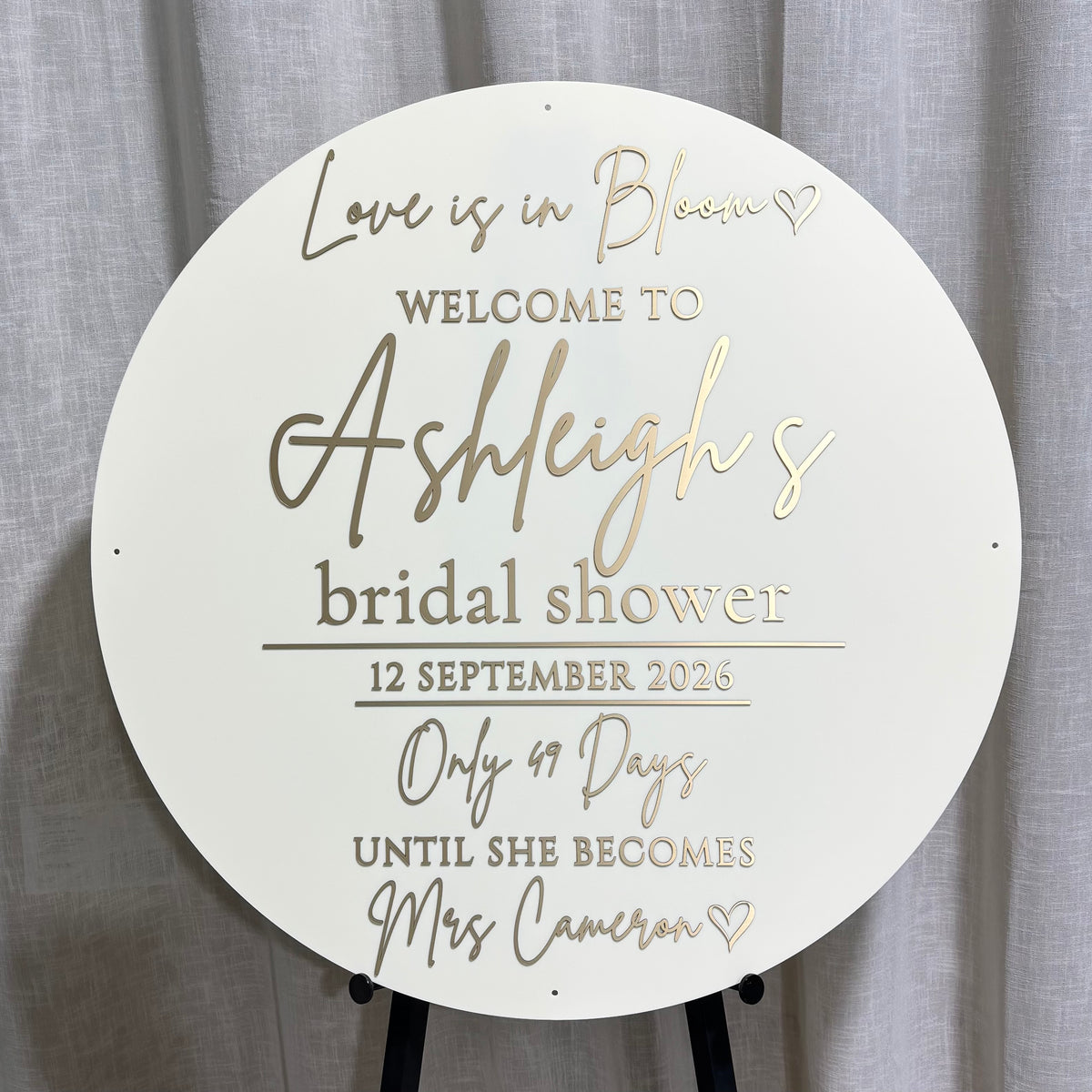 Large round white acrylic bridal shower welcome sign featuring mirror gold acrylic lettering and engraved details, personalised with the bride’s name, event date and countdown, creating an elegant wedding and bridal shower entrance display.