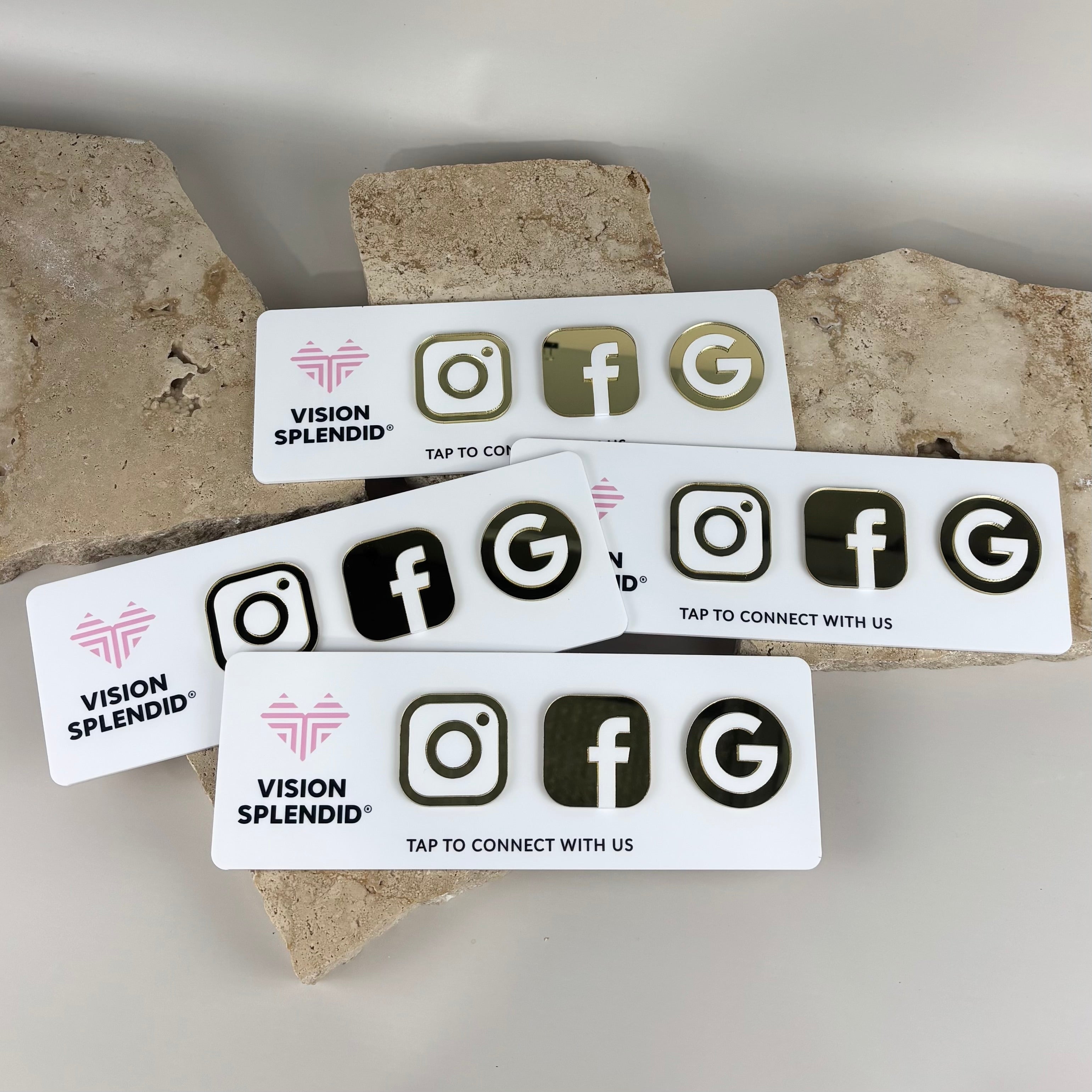 Custom white acrylic NFC social media tap cards for Vision Splendid, featuring 3D gold Instagram, Facebook and Google icons with “Tap to connect with us” text, displayed on stone backdrop.