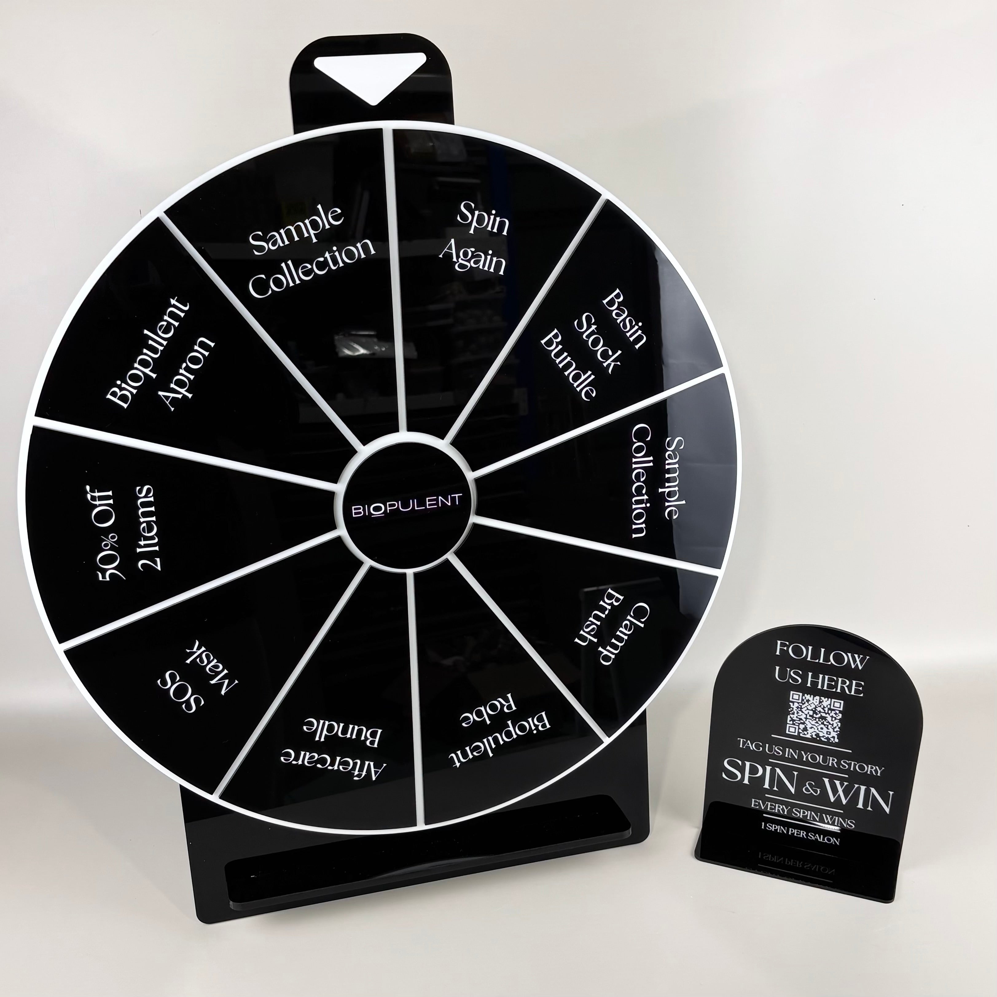 Custom acrylic spin the wheel prize game for salons, beauty clinics, retail stores, trade shows and promotional events. Branded prize wheel featuring custom rewards, QR code signage and interactive customer engagement marketing designed to increase social media follows, customer participation, brand awareness and sales.