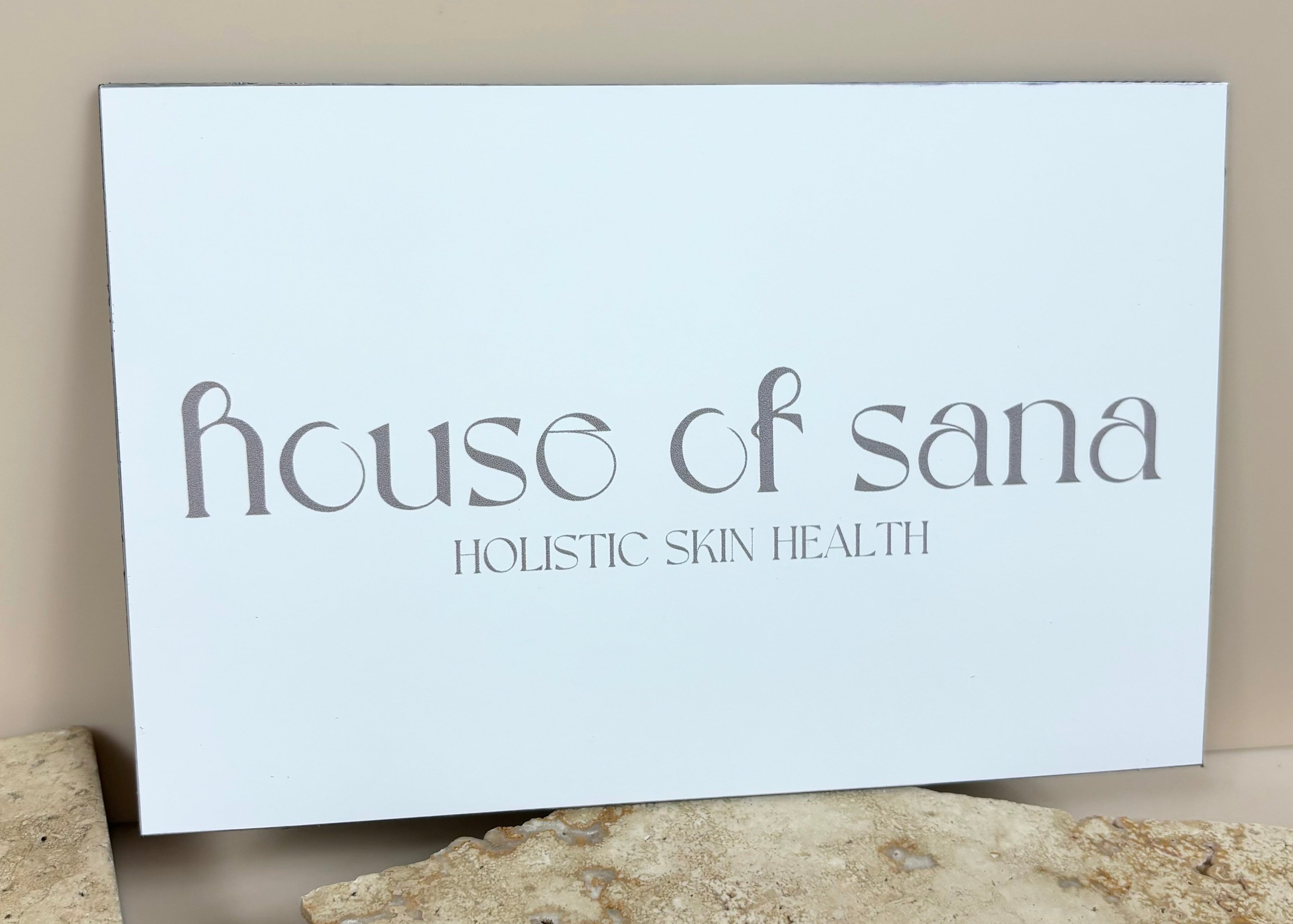 House of Sana wall-mounted business sign, sleek aluminium panel printed with modern branding for a skincare clinic.