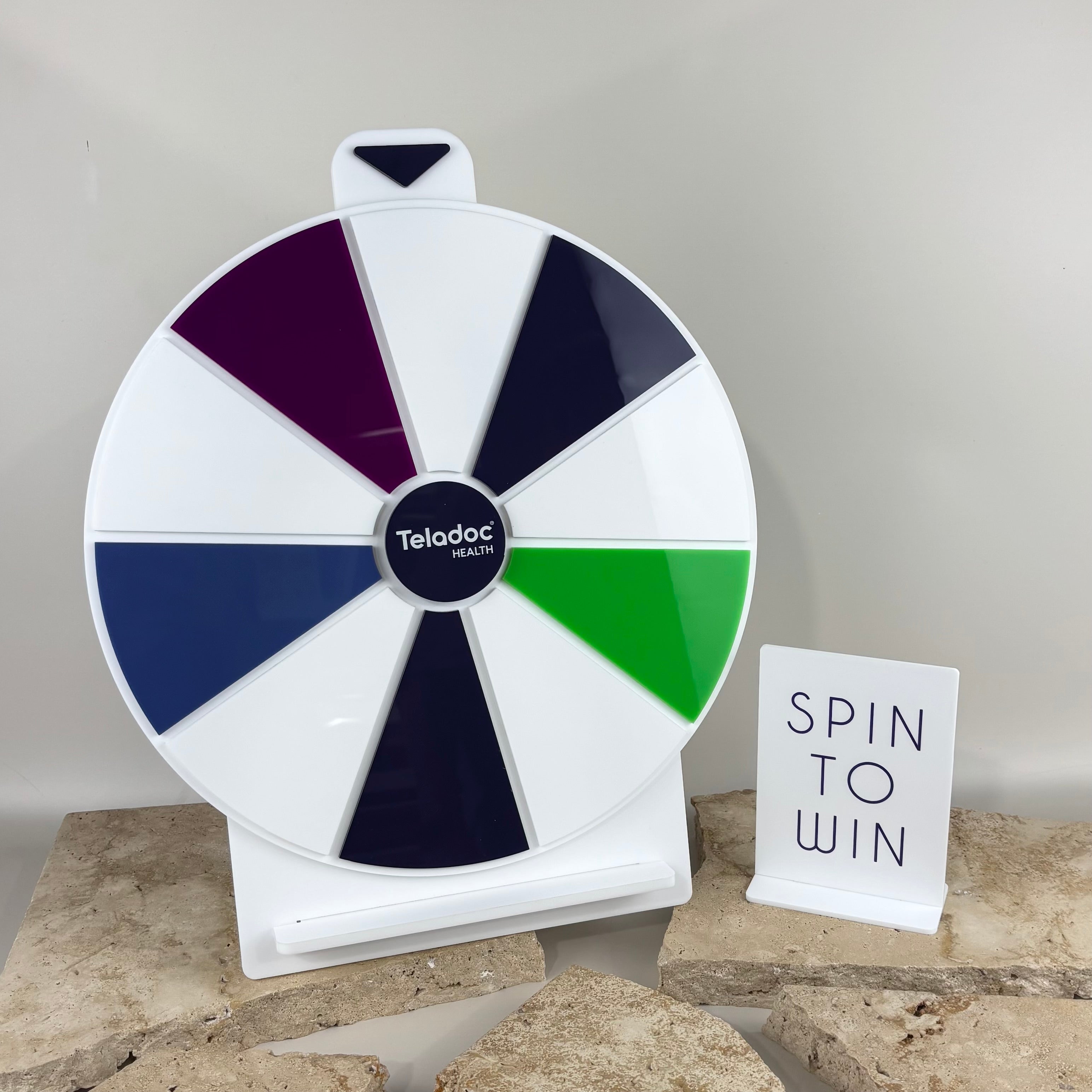 Custom branded spin to win prize wheel with Teladoc Health logo, white acrylic display with coloured segments, promotional marketing game for events, salons and retail businesses, freestanding countertop spinner Australia.