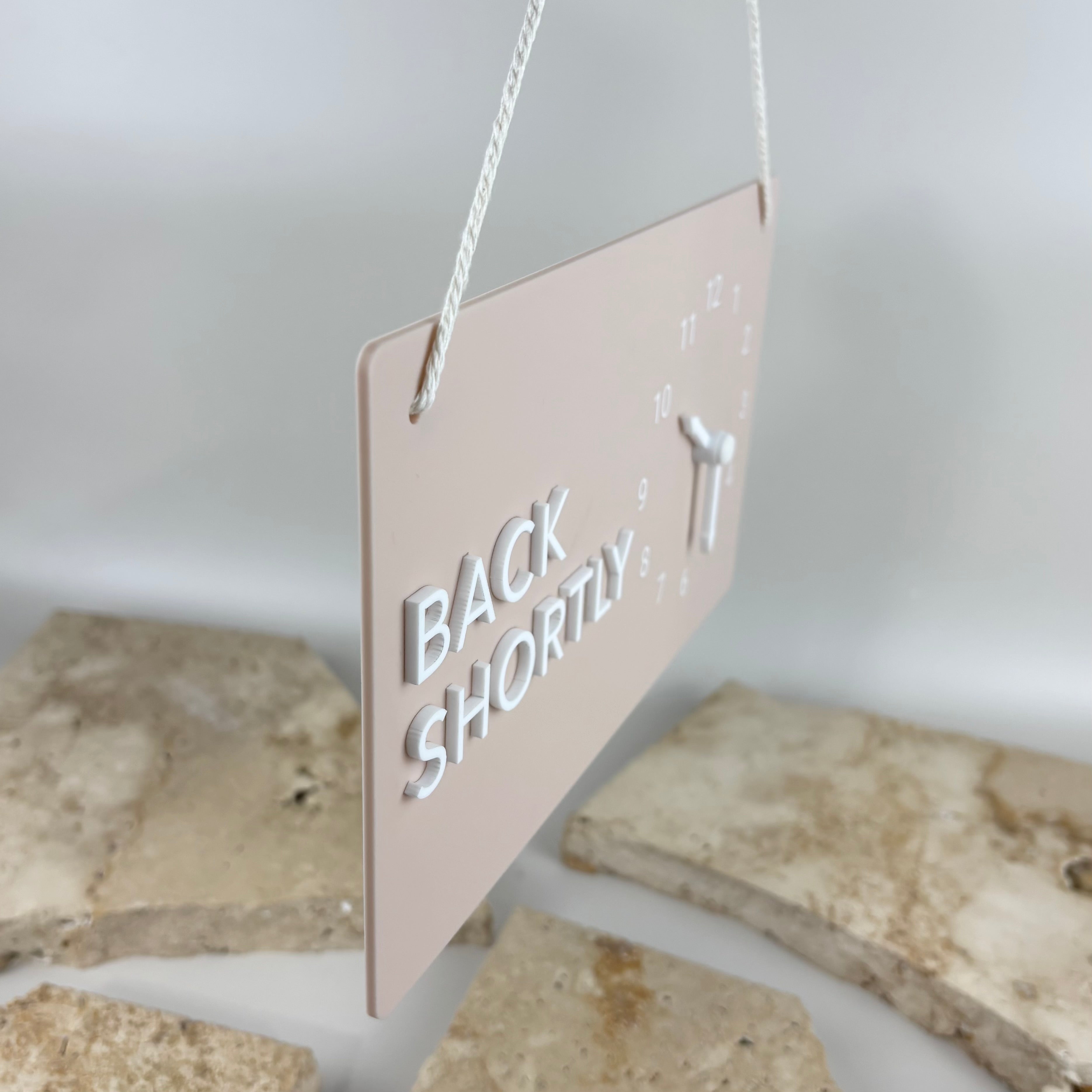 Side view of acrylic Back Shortly business door sign with raised 3D lettering, movable return time clock hands and hanging rope.