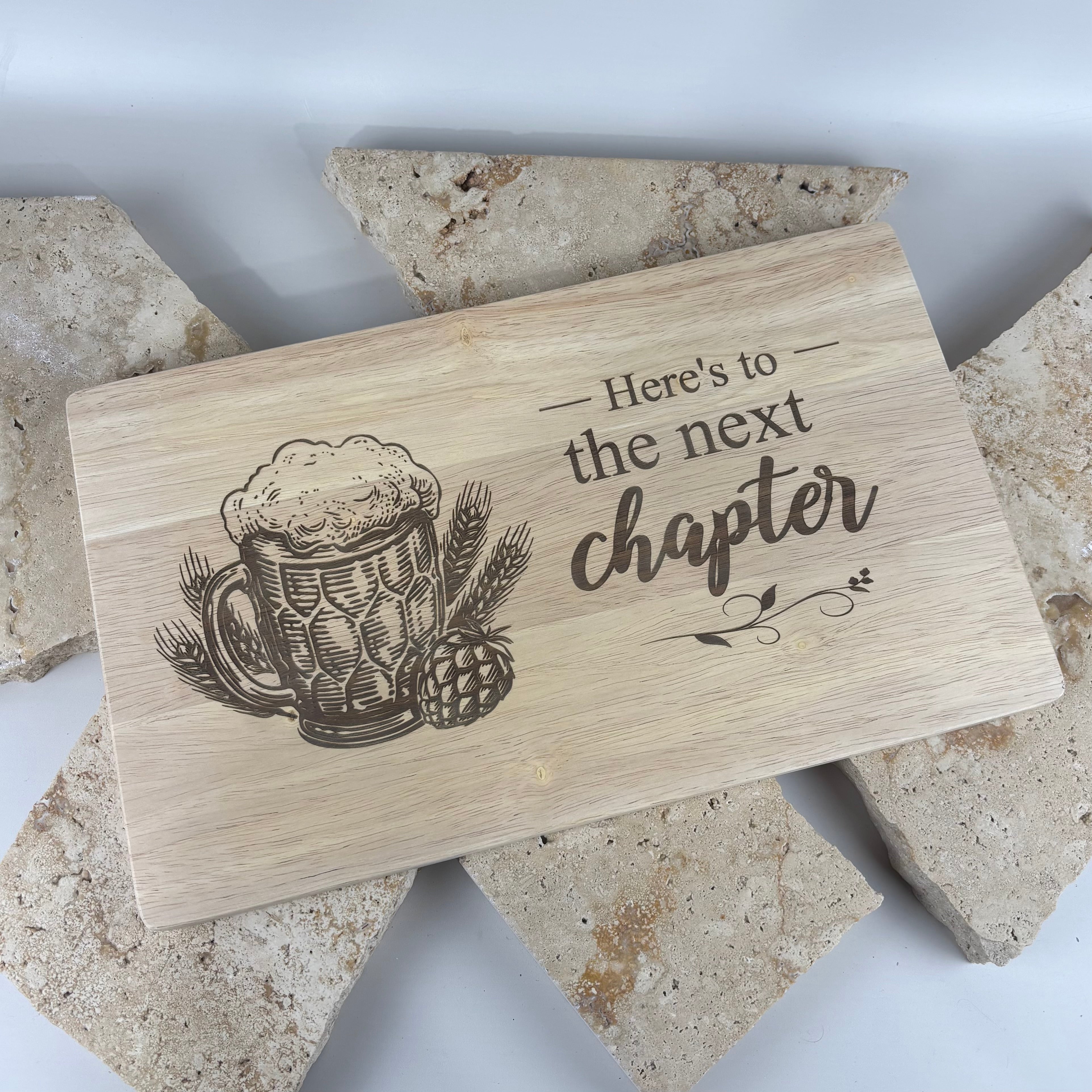 Custom laser engraved wooden serving board featuring a personalised beer mug design and the message “Here’s to the next chapter”. Premium rubberwood chopping and grazing board, perfect as a retirement gift, farewell gift, Father’s Day gift, housewarming present or personalised keepsake.