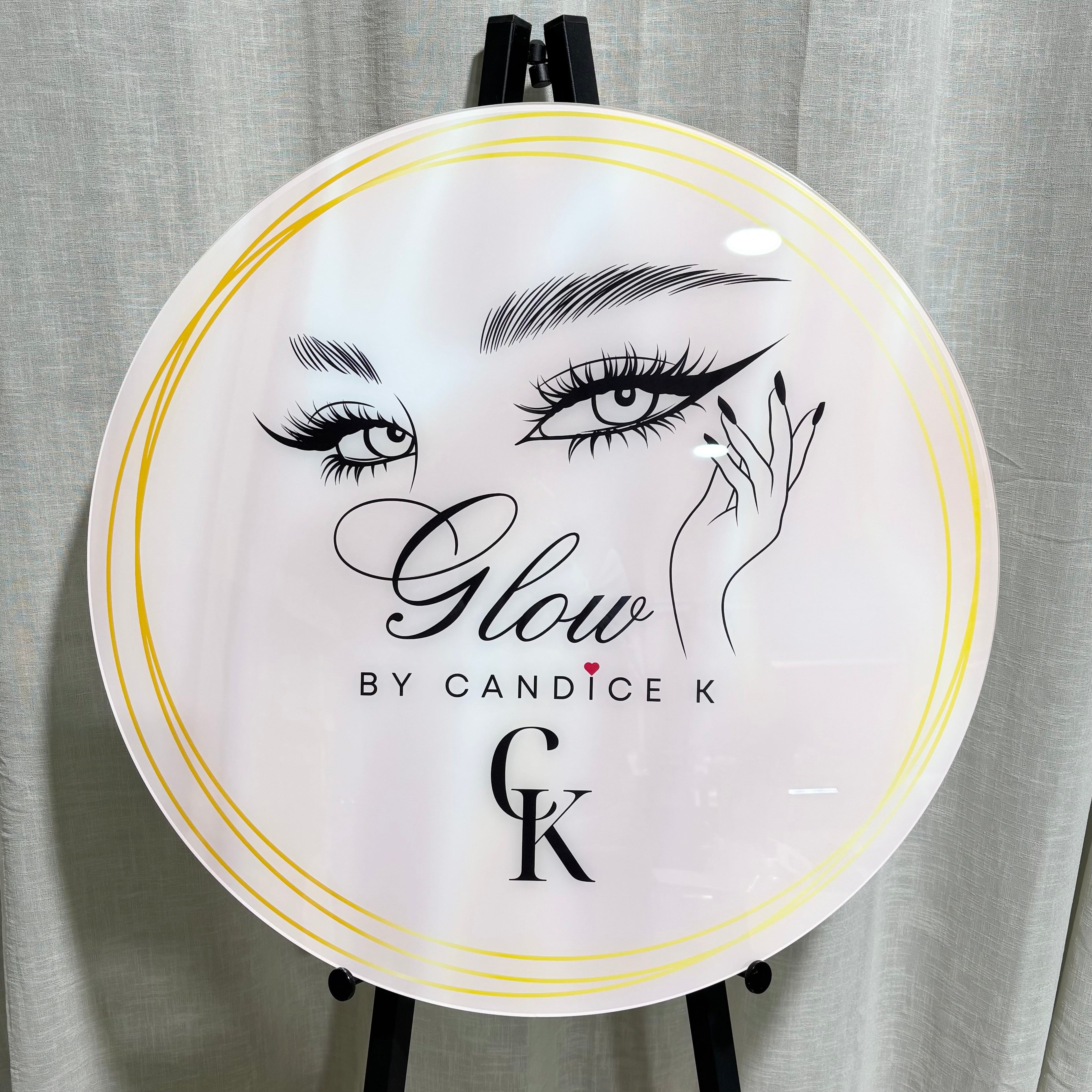 Round UV printed acrylic business sign for Glow by Candice K featuring elegant lash and brow artwork, gold ring border, and black logo text CK – custom salon signage by Laser Edge Designs Australia.