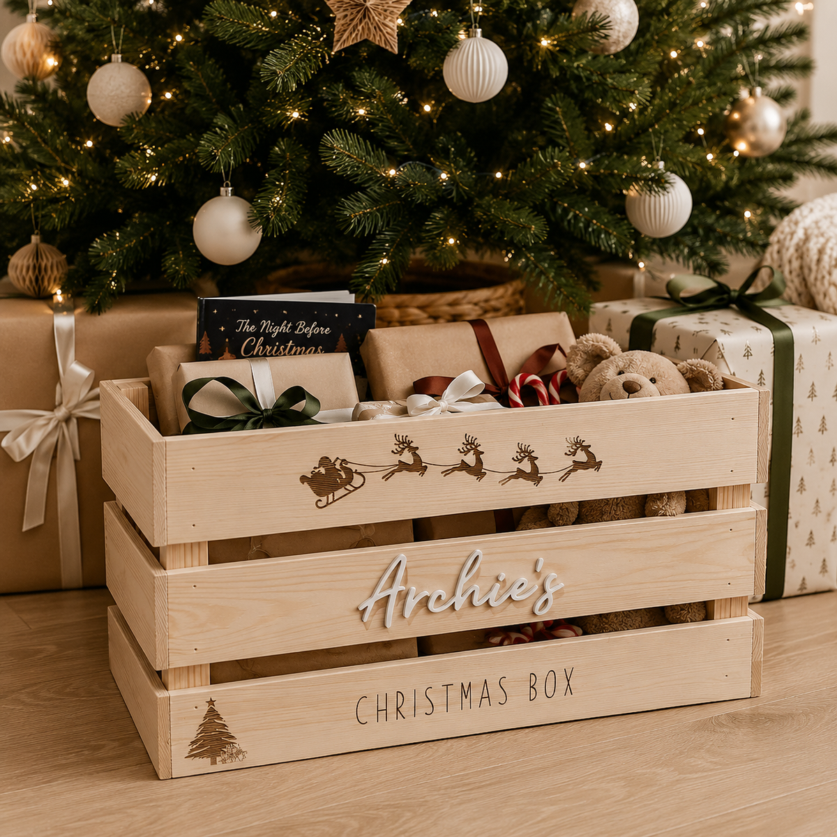 Personalised wooden Christmas Eve box under a modern Christmas tree, filled with wrapped presents, a Christmas book, teddy bear and festive treats. Rustic timber Christmas crate for family Christmas Eve traditions.