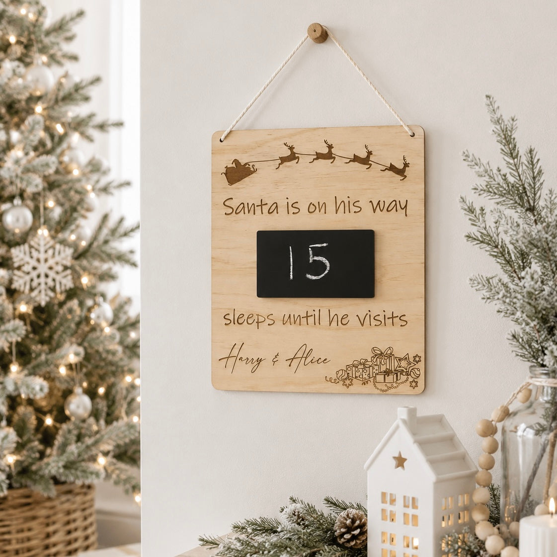 Personalised wooden Santa Christmas countdown plaque with chalkboard number display, hanging in a light modern Christmas setting beside a decorated tree and festive décor.
