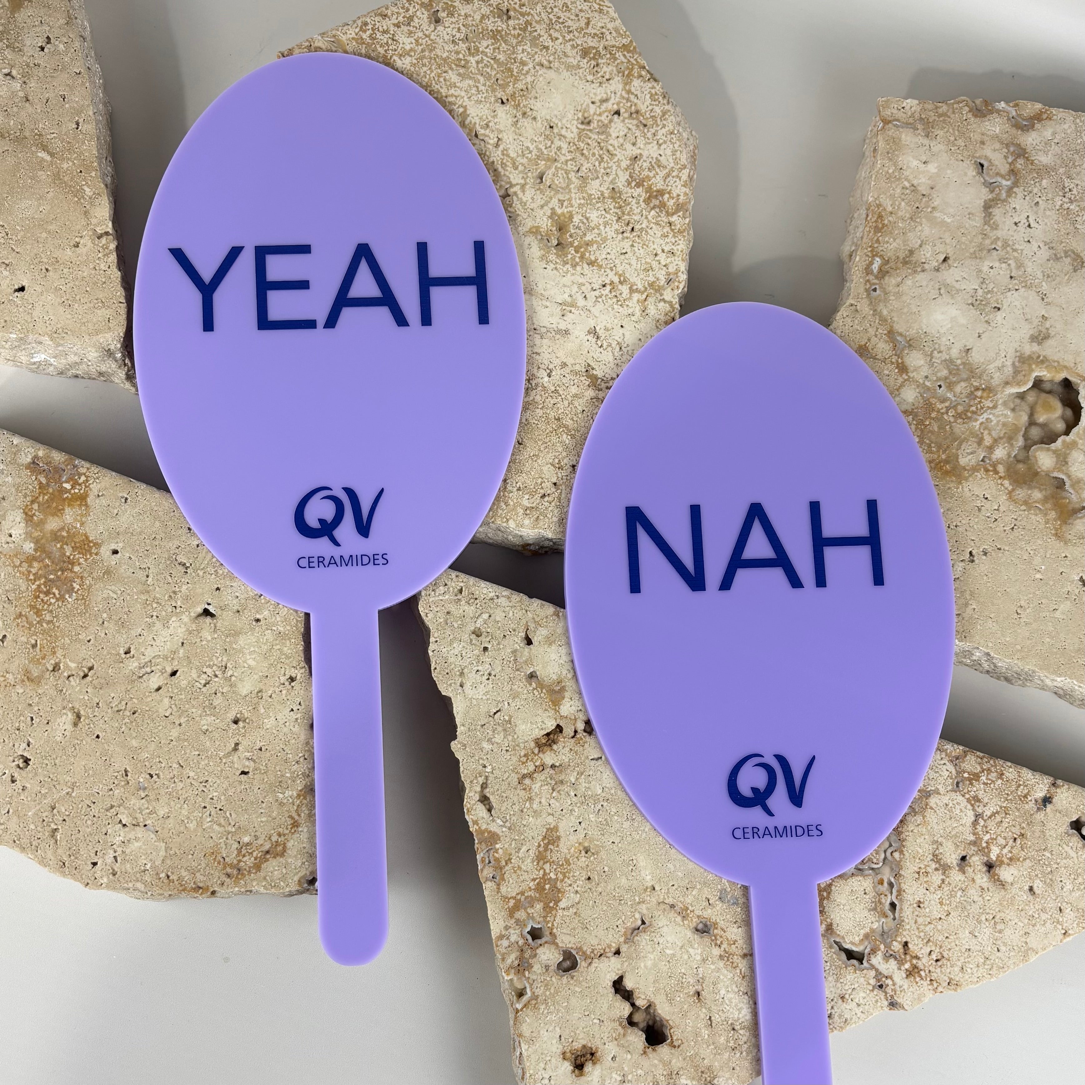 Purple acrylic yes and no paddles branded with QV Ceramides, featuring “yeah” and “nah” text, ideal for skincare events, promotions and interactive client engagement.