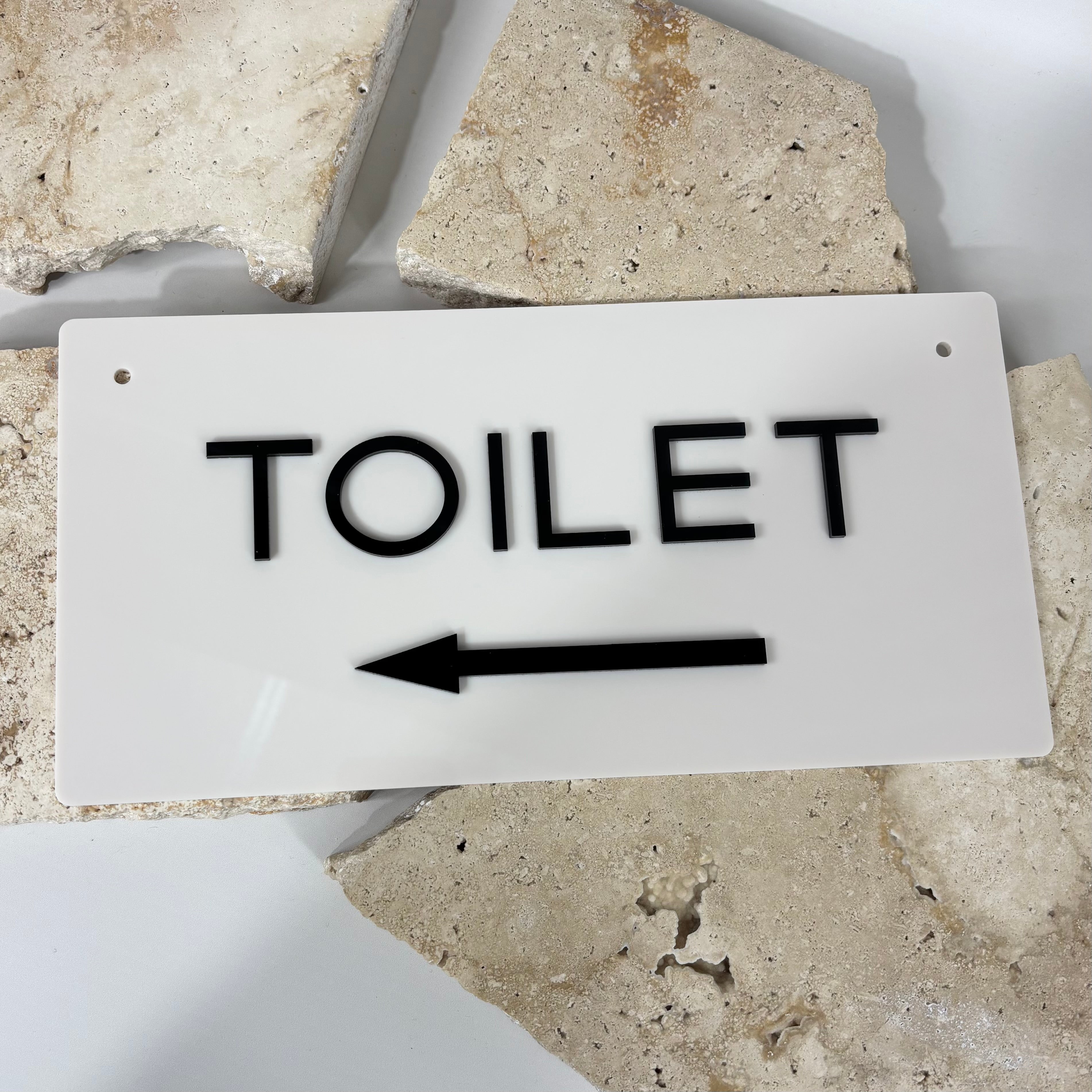Modern 3D acrylic toilet direction sign in white with raised black lettering and left-pointing arrow, 30x15cm bathroom wall sign made in Australia by Laser Edge Designs.