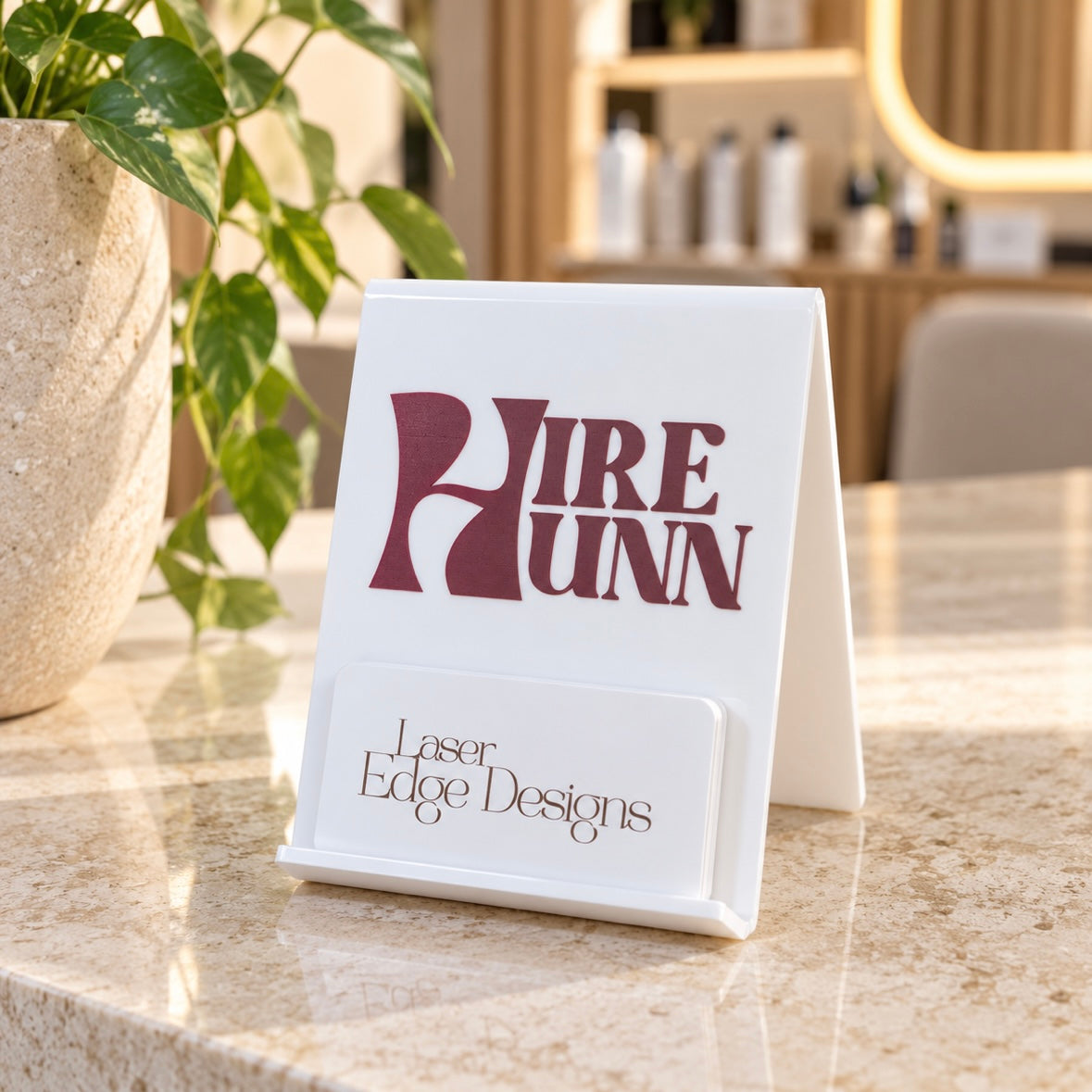 Custom white acrylic A-frame business card holder with raised burgundy logo and branded card display, styled on a modern reception counter.