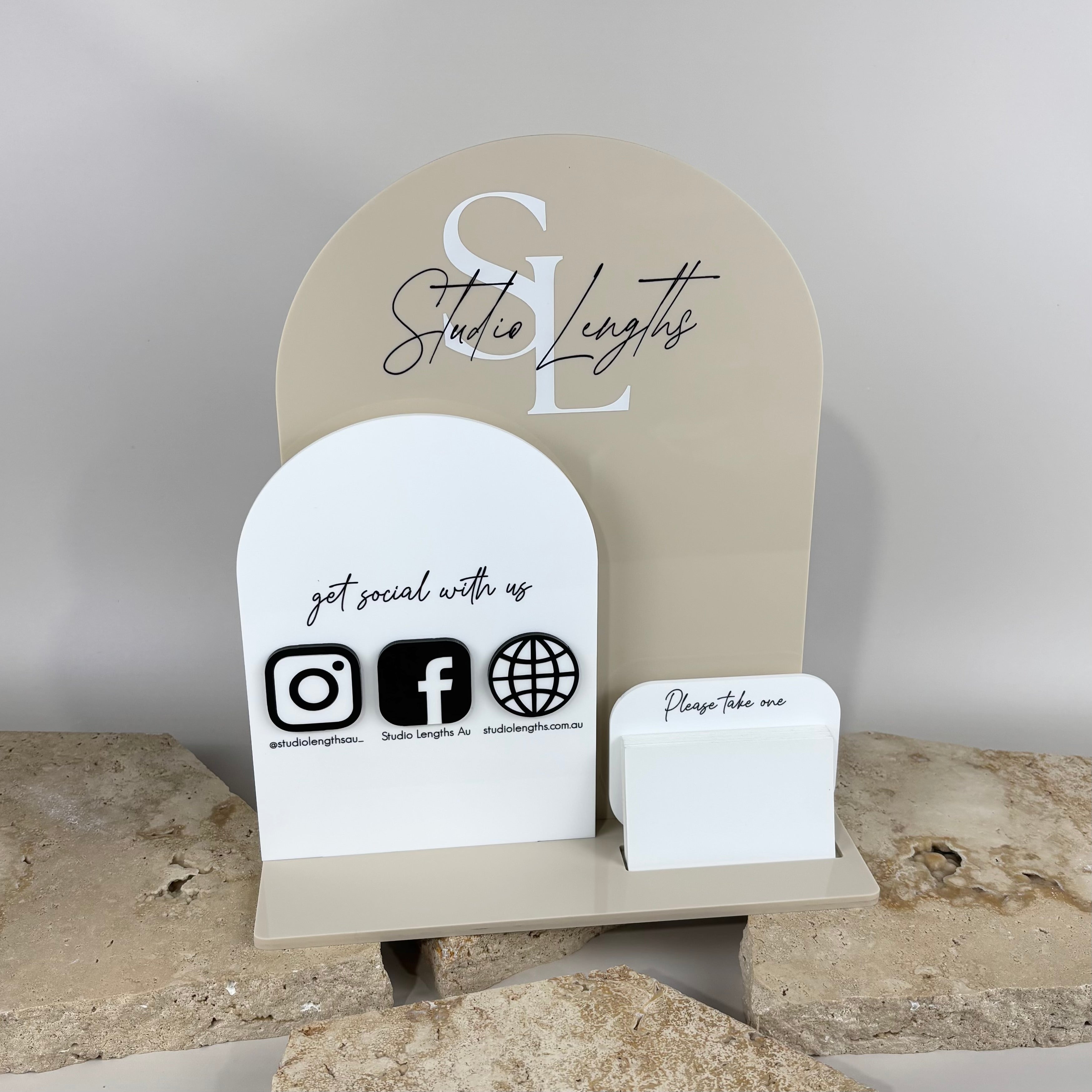 Custom acrylic business counter display for Studio Lengths, featuring a beige arch sign with logo, white social media panel with Instagram, Facebook and website icons, and a matching business card holder, styled on natural stone tiles.