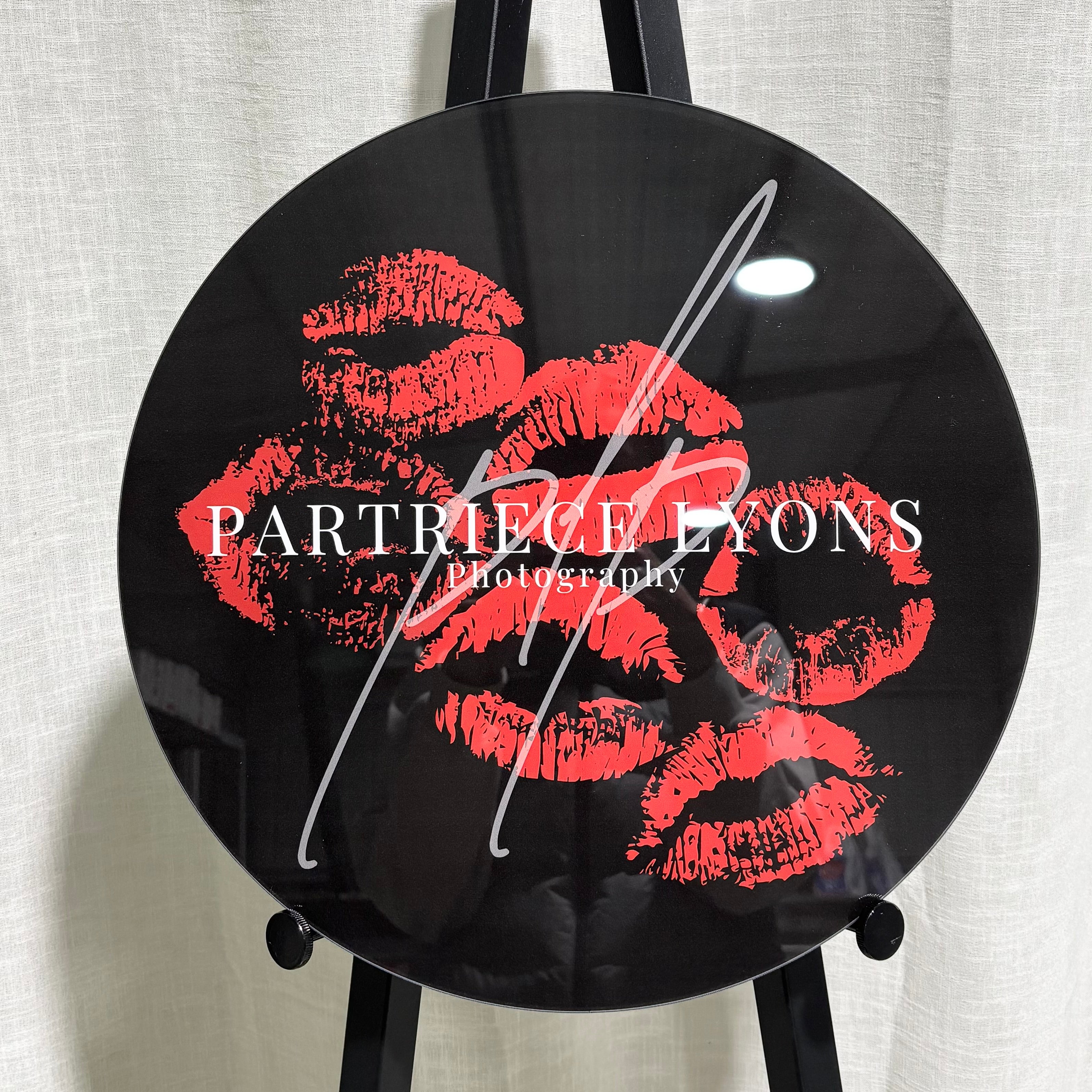 Custom round black acrylic photography sign with bold red lipstick kiss prints and white Partriece Lyons Photography logo, perfect for professional studio branding and event displays