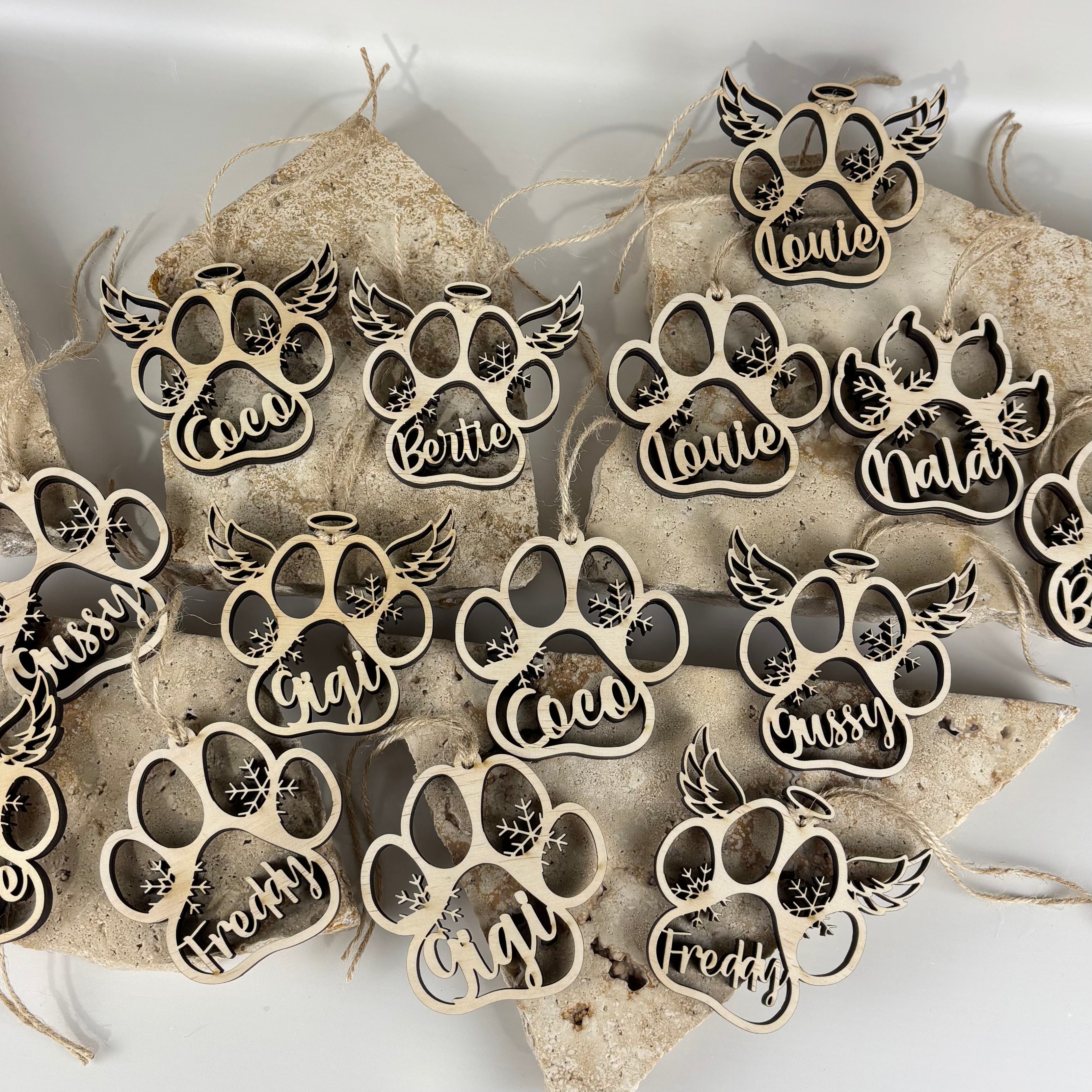 personalised pet memorial christmas ornaments shaped as paw prints with angel wings displayed on stone background, custom engraved pet names coco gigi louie nala bertie freddy, laser cut wooden paw baubles remembrance keepsake australia made