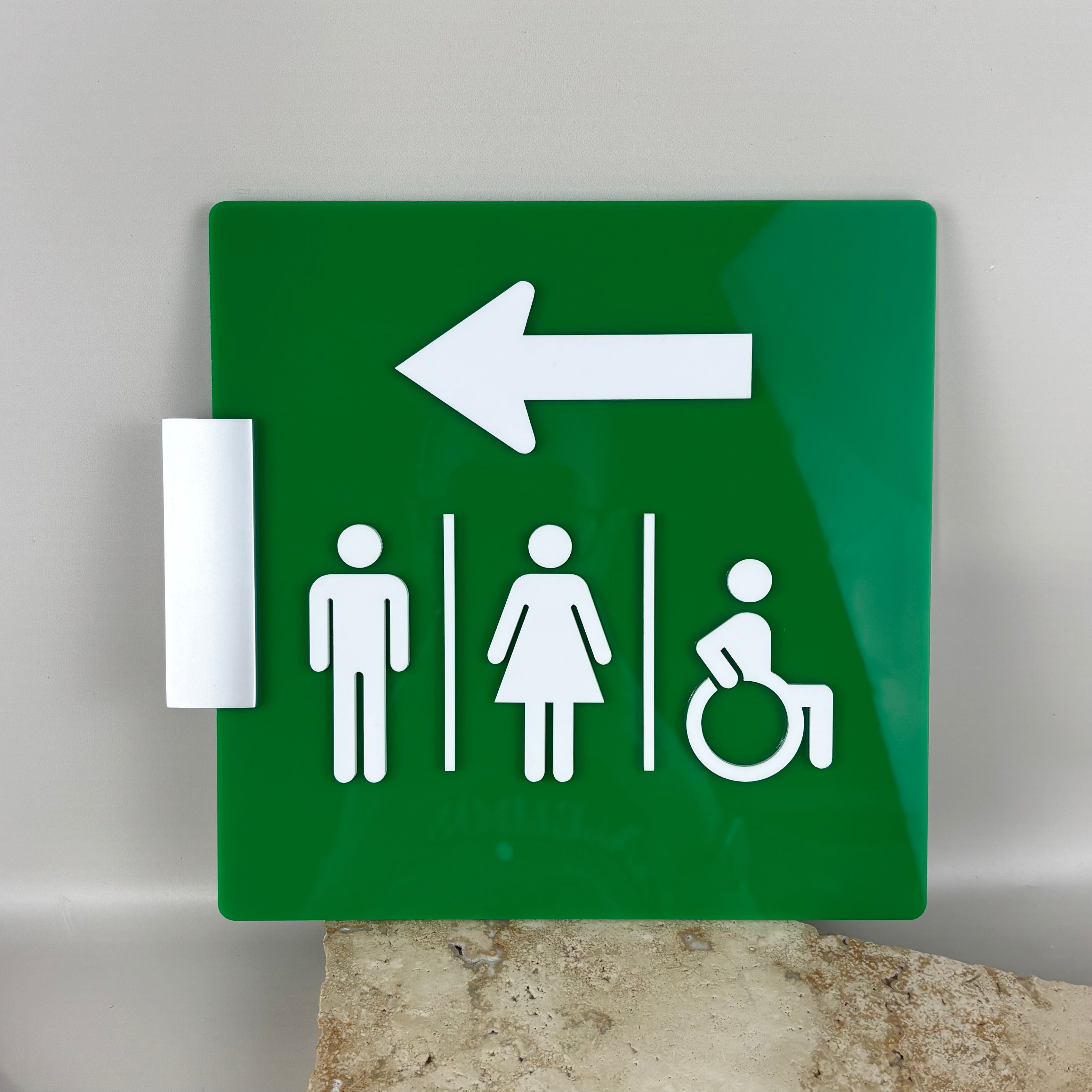 Green acrylic corridor sign with white directional arrow and male, female and wheelchair accessibility restroom symbols, designed for commercial hallway and bathroom wayfinding