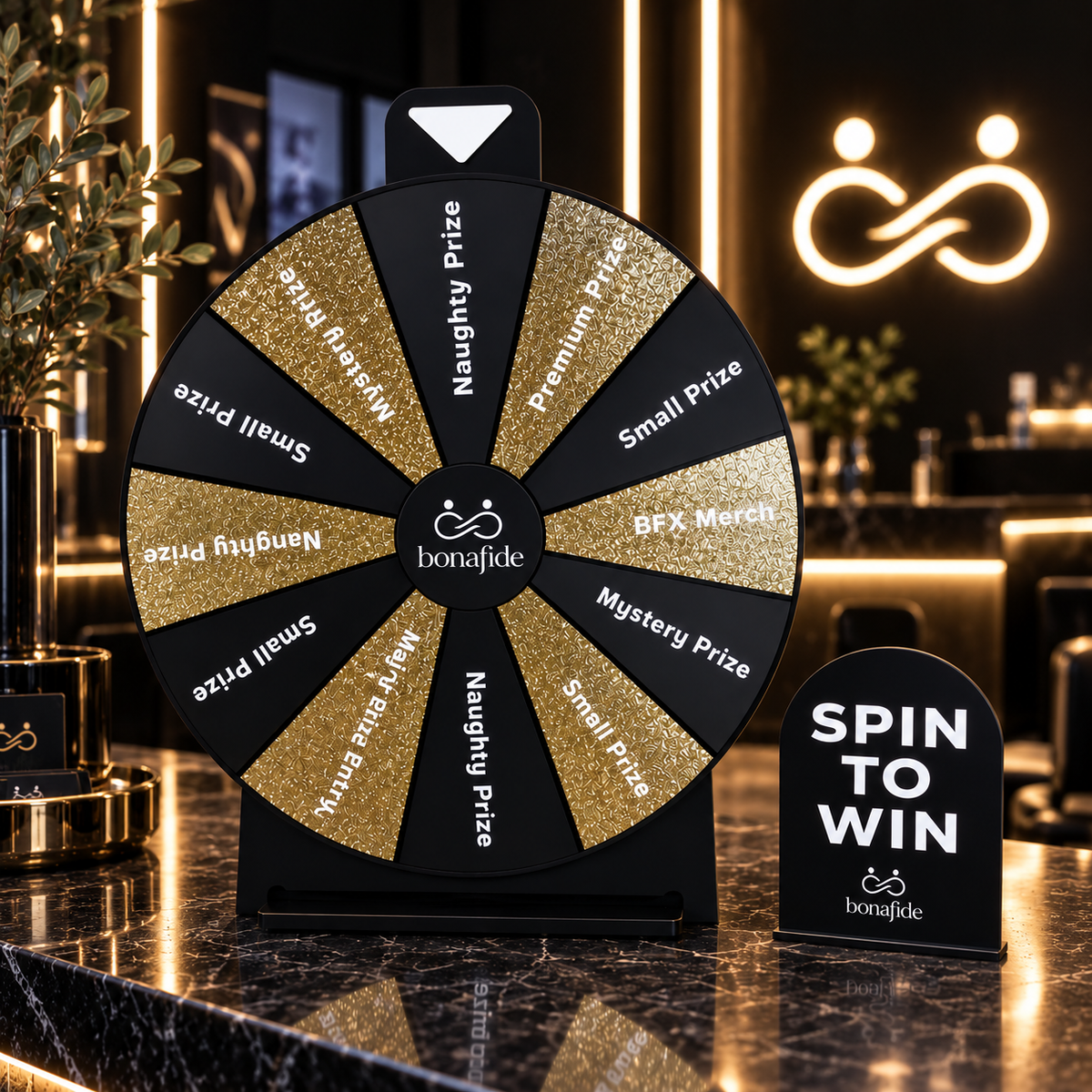 Custom black and gold glitter acrylic Spin to Win prize wheel with personalised Bonafide branding and prizes, displayed with a matching countertop sign in a luxury event setting.