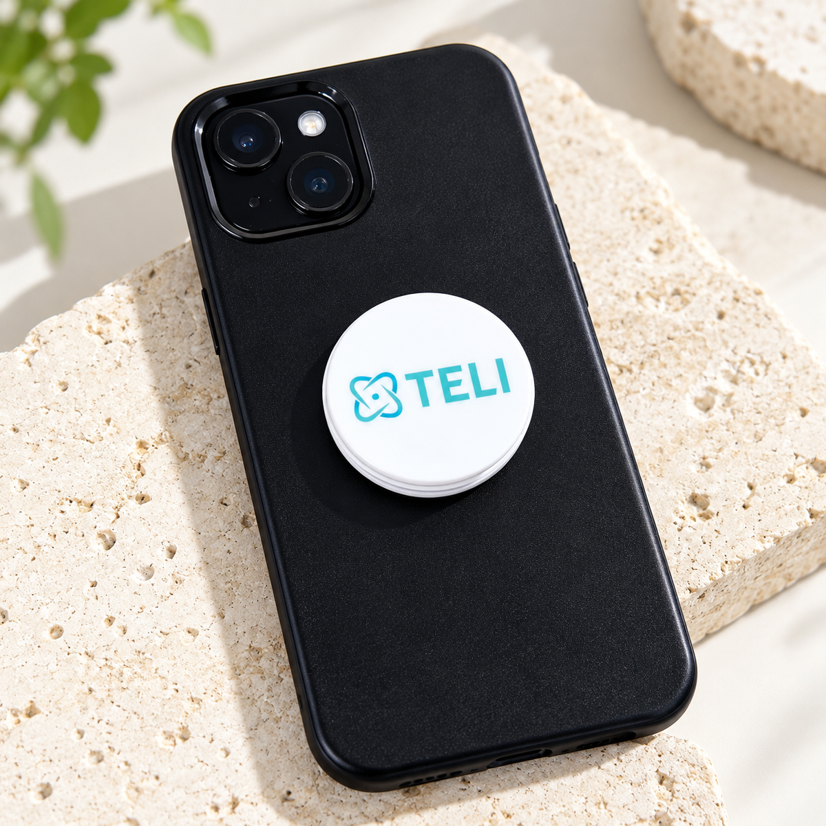 Custom white phone grip with turquoise TELI business logo attached to a smartphone, held by a woman in a modern workspace.