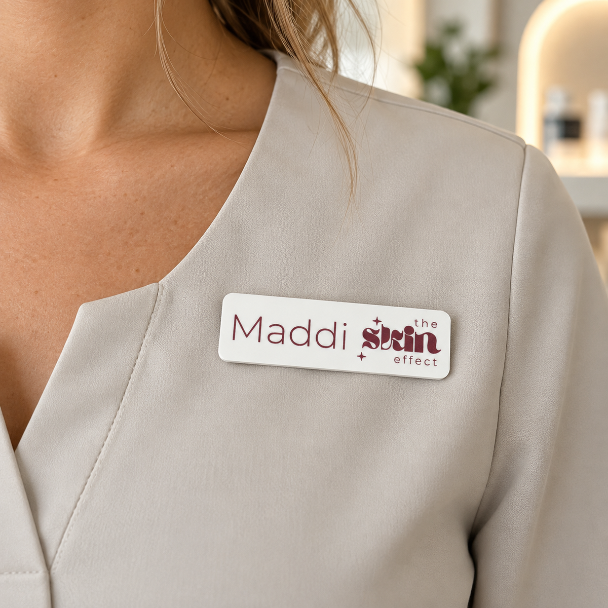 Custom white acrylic magnetic name badge featuring Maddi and The Skin Effect branding in burgundy, worn on a cream beauty clinic uniform.