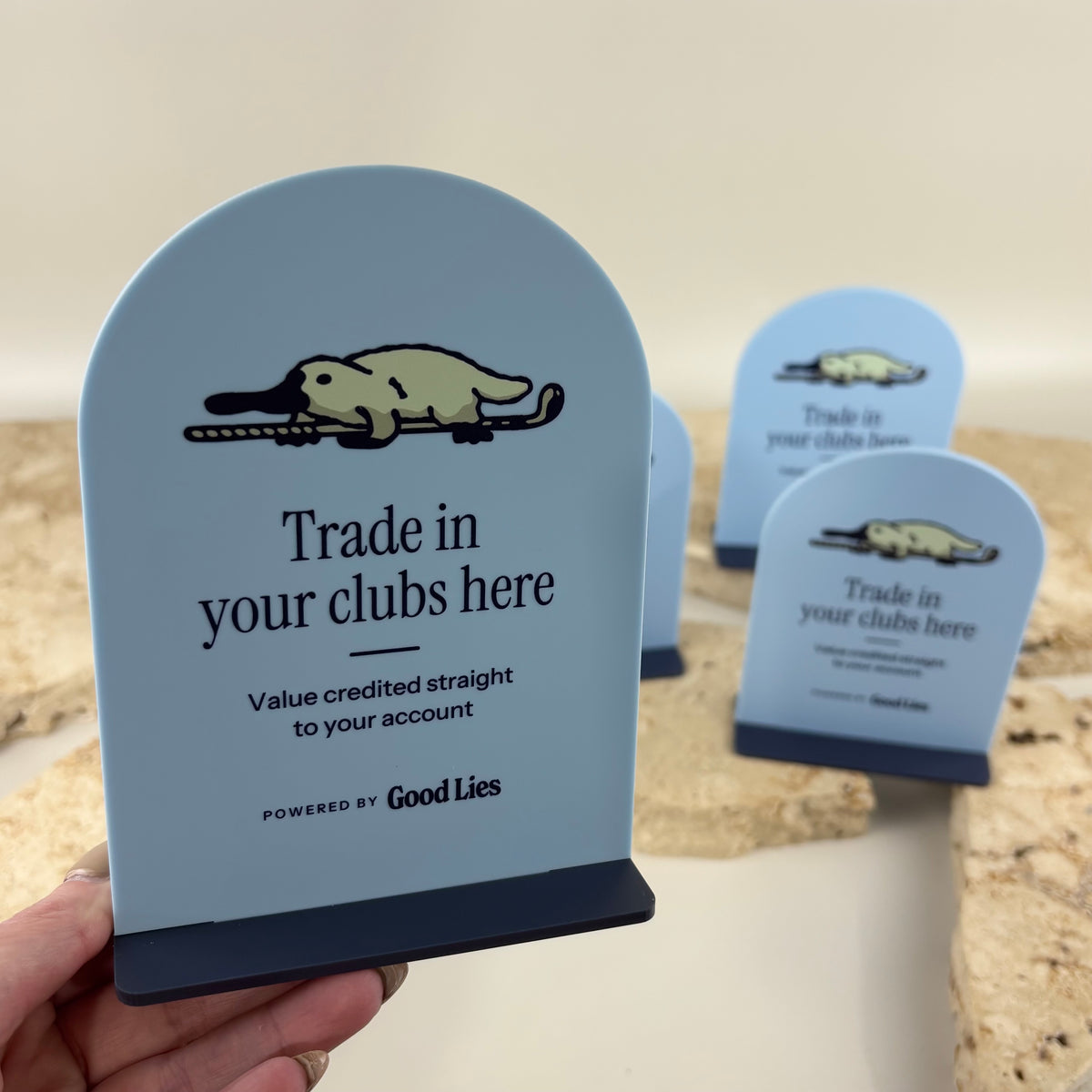 Custom mini arched acrylic countertop display signs in light blue with navy bases, featuring Good Lies golf club trade-in branding and printed business information.