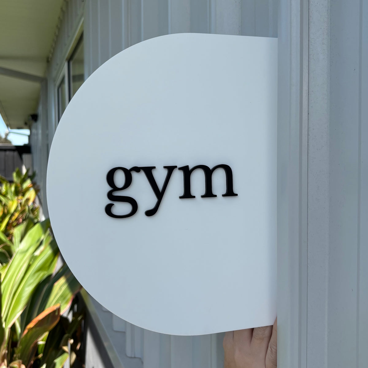 White round acrylic blade sign with raised black 3D gym lettering, designed as a modern double-sided business sign for a fitness studio.