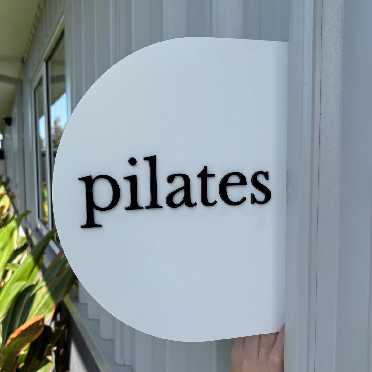 Custom white round acrylic blade sign with raised black 3D pilates lettering, ideal for pilates studios, wellness businesses and fitness studio entrances.