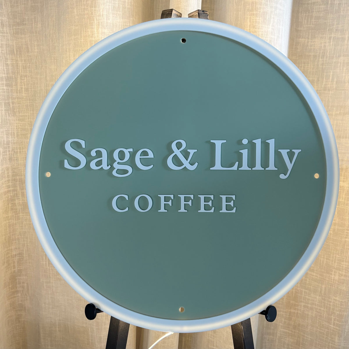 Custom round LED backlit acrylic cafe sign for Sage & Lilly Coffee, featuring a sage green face, raised white 3D lettering and illuminated white border.