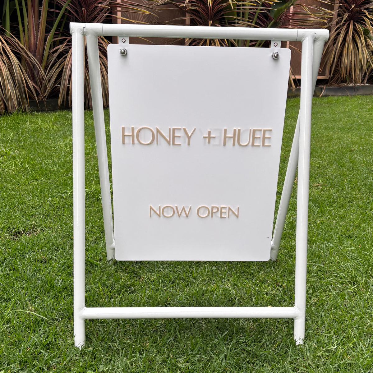 Custom white swing pavement sign with 3D acrylic lettering for Honey + Hue, displayed outdoors.