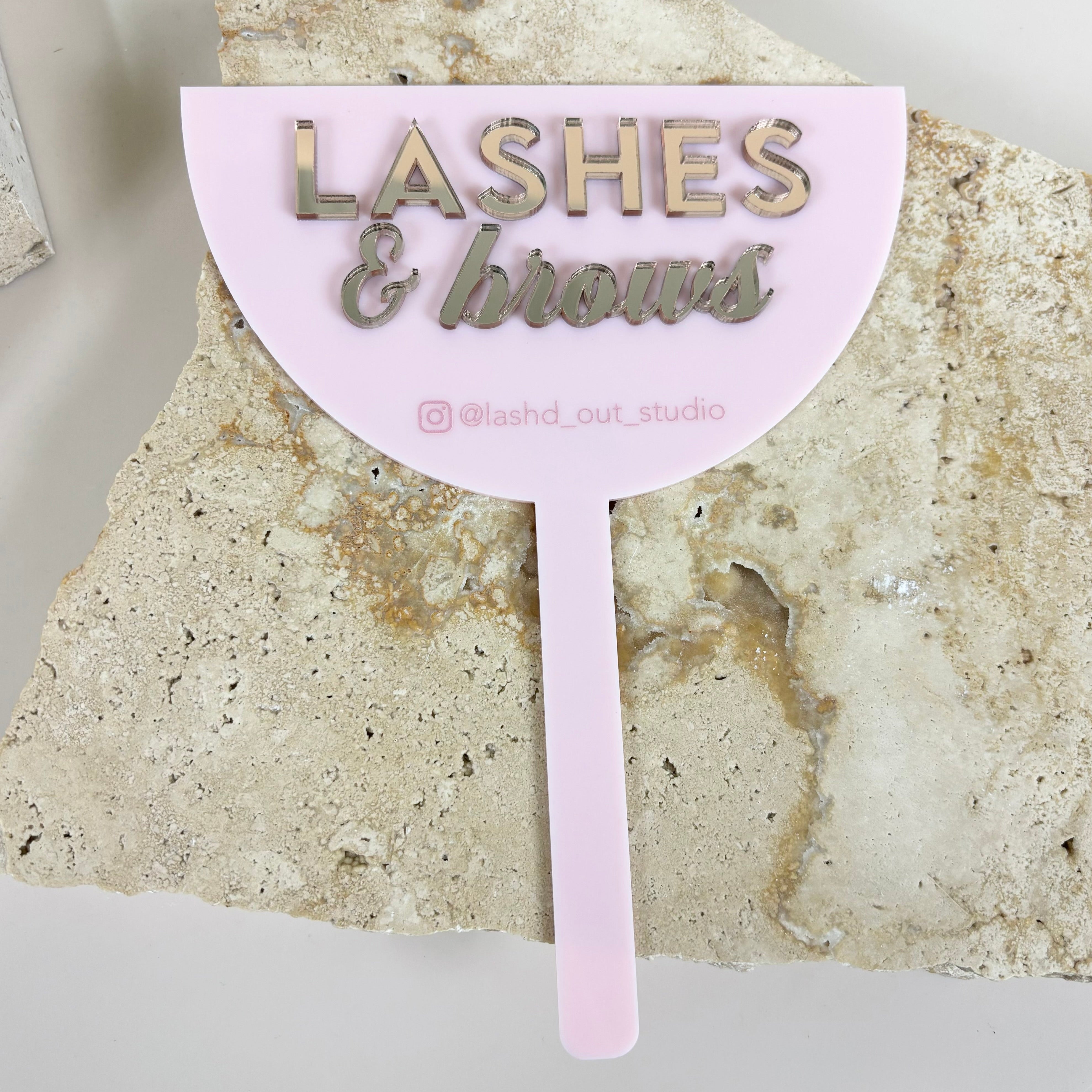 Pink branded 3D face shield with Lashes and Brows logo displayed on stone background