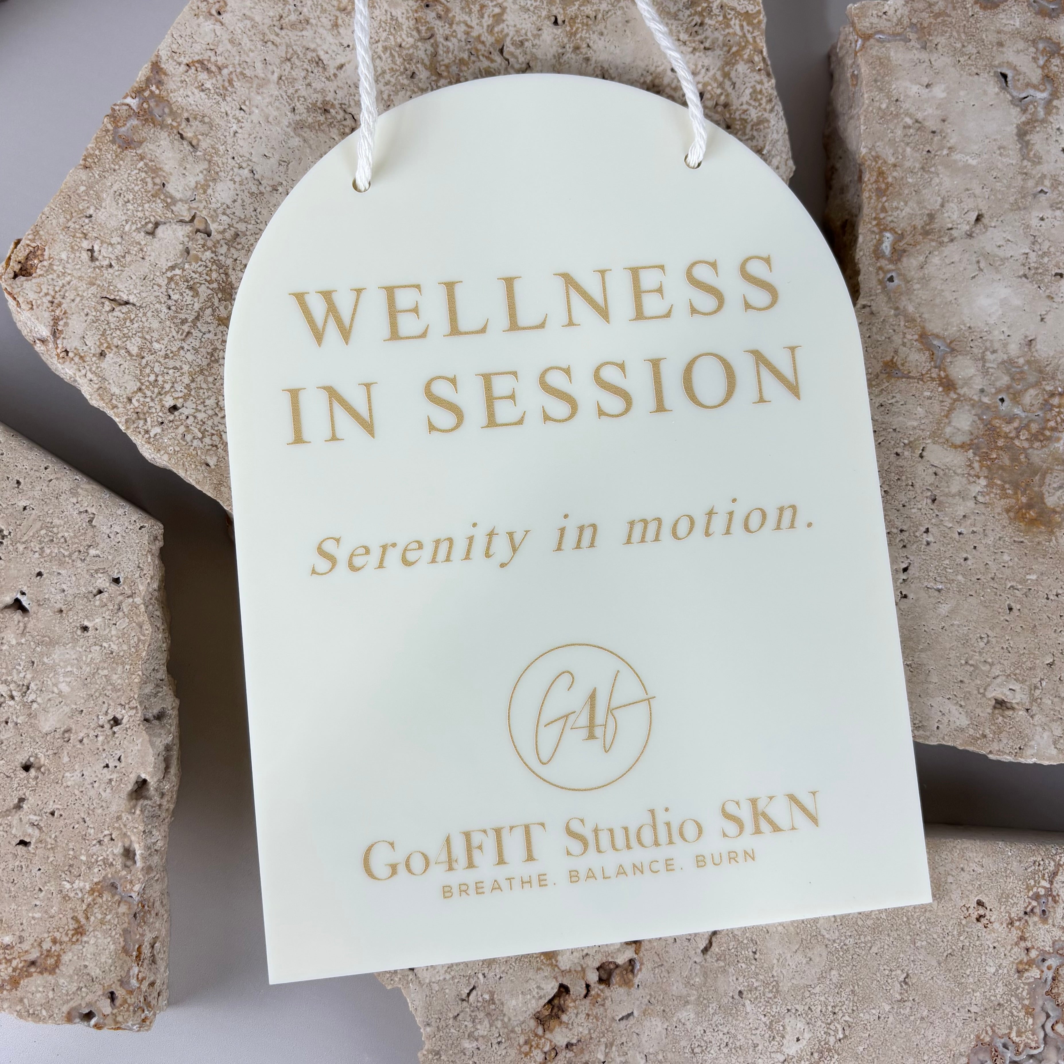 cream acrylic wellness studio door sign with rope hanger reading “wellness in session, serenity in motion,” custom gold lettering spa and treatment room signage australia