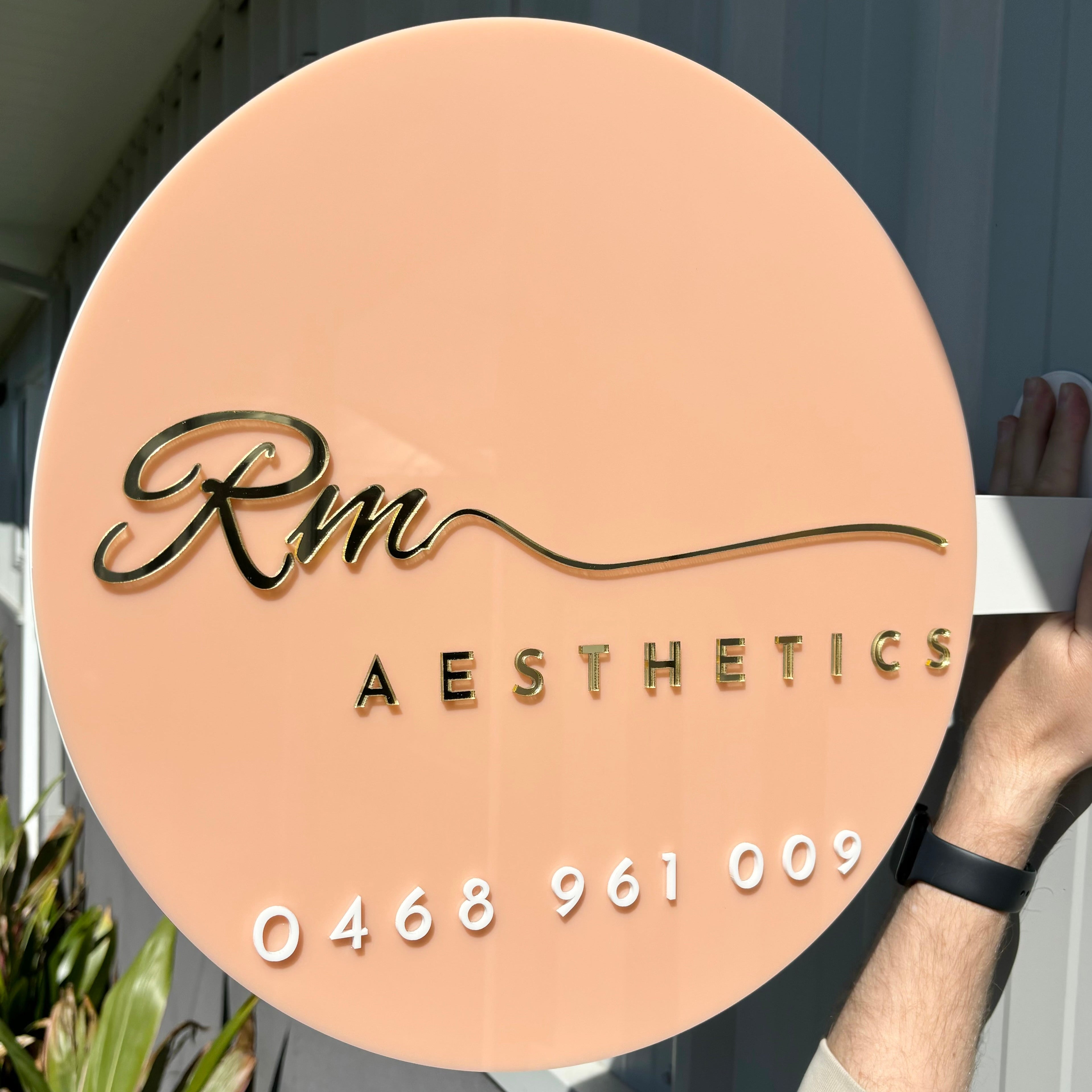 Peach-toned business sign for RM Aesthetics with phone number