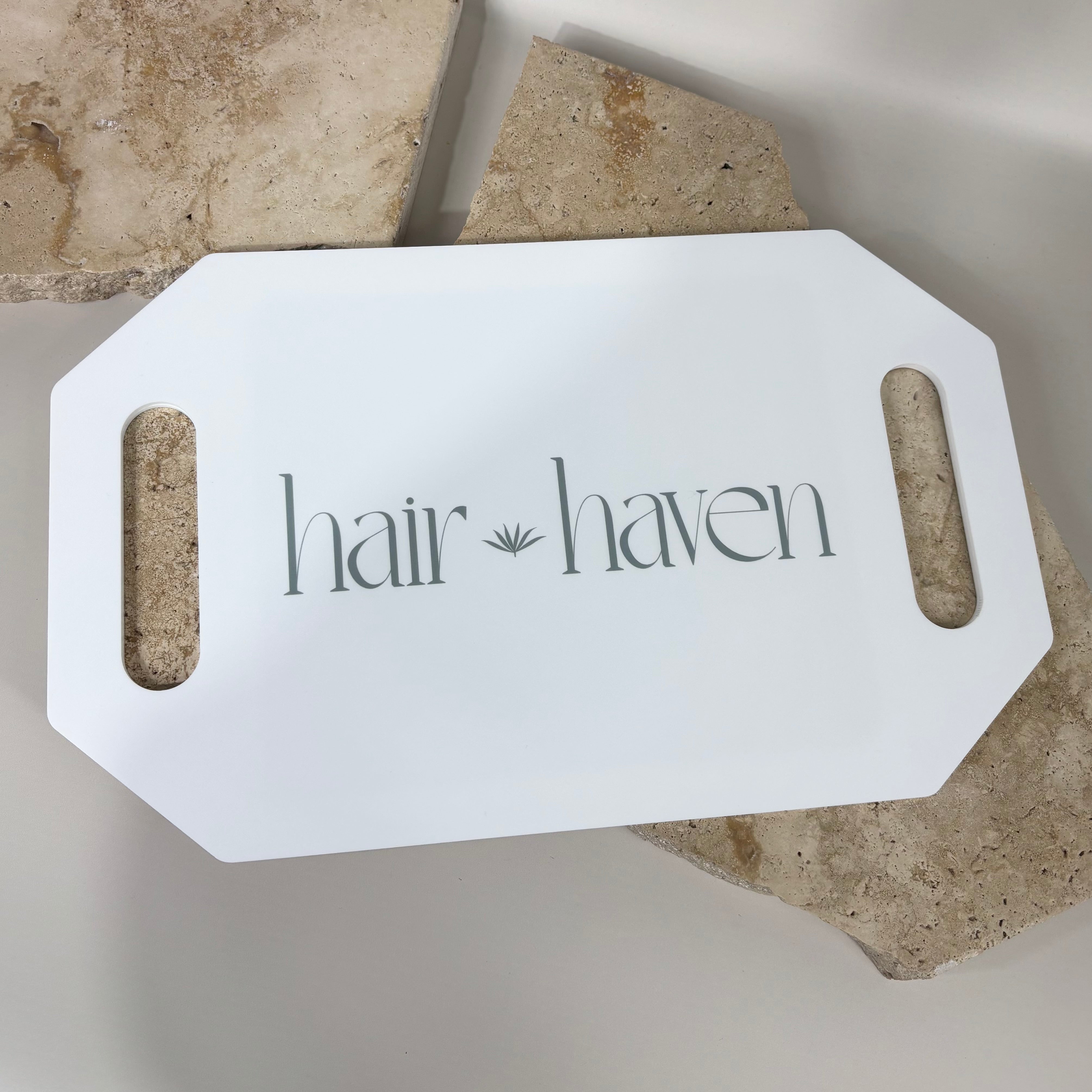 White acrylic salon tray with cut-out handles, custom printed with “Hair Haven” logo in grey, displayed on textured stone background.