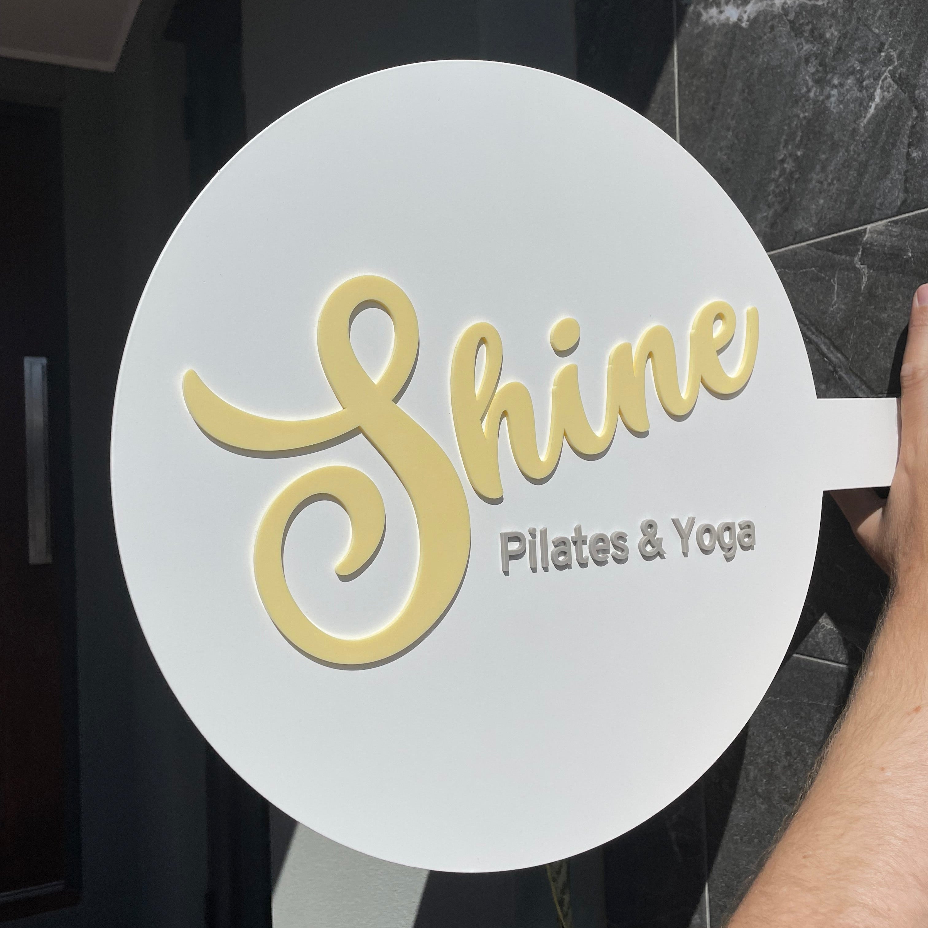 Shine Pilates & Yoga round sign with yellow script font