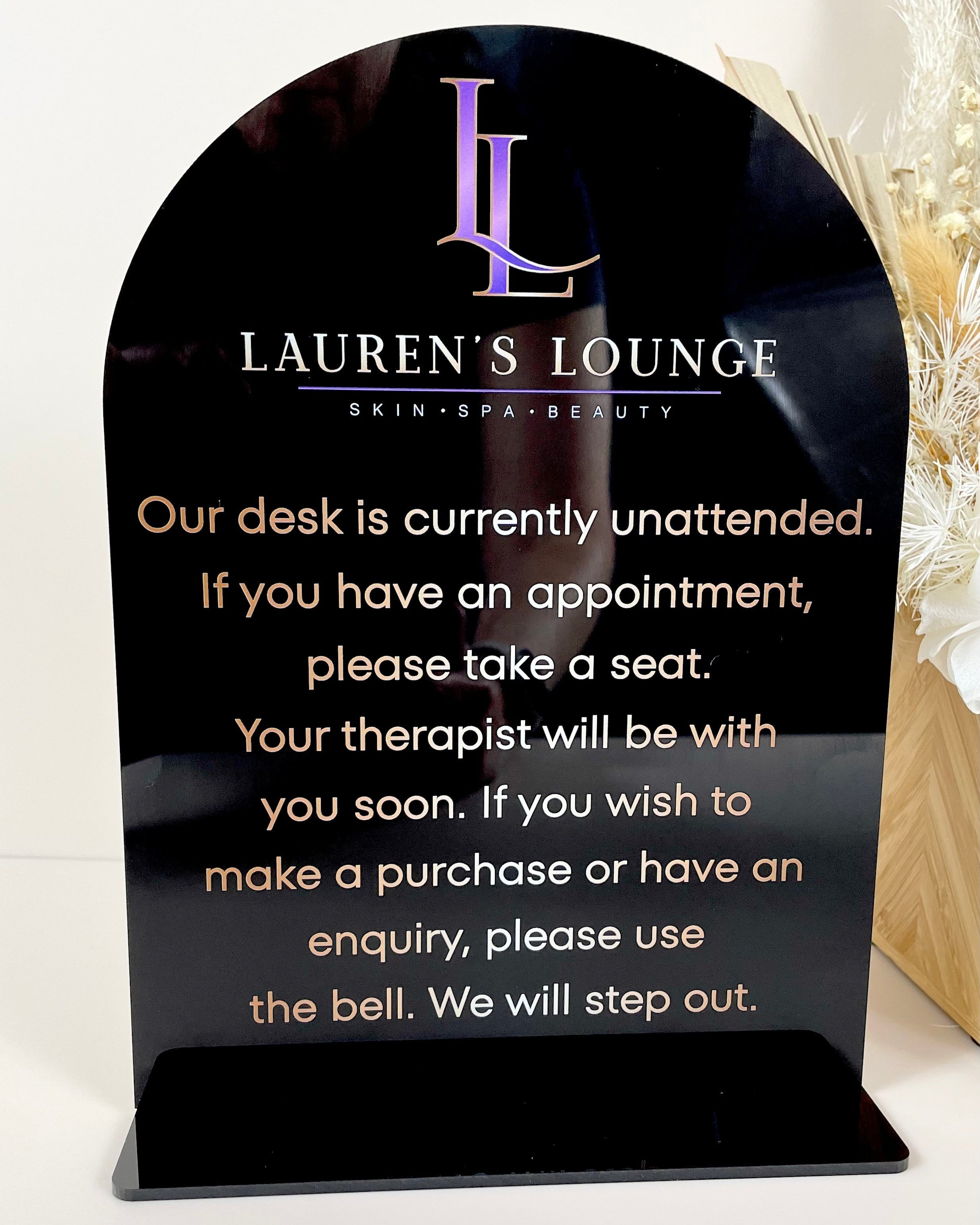 Black acrylic counter sign with white and purple text for beauty lounge