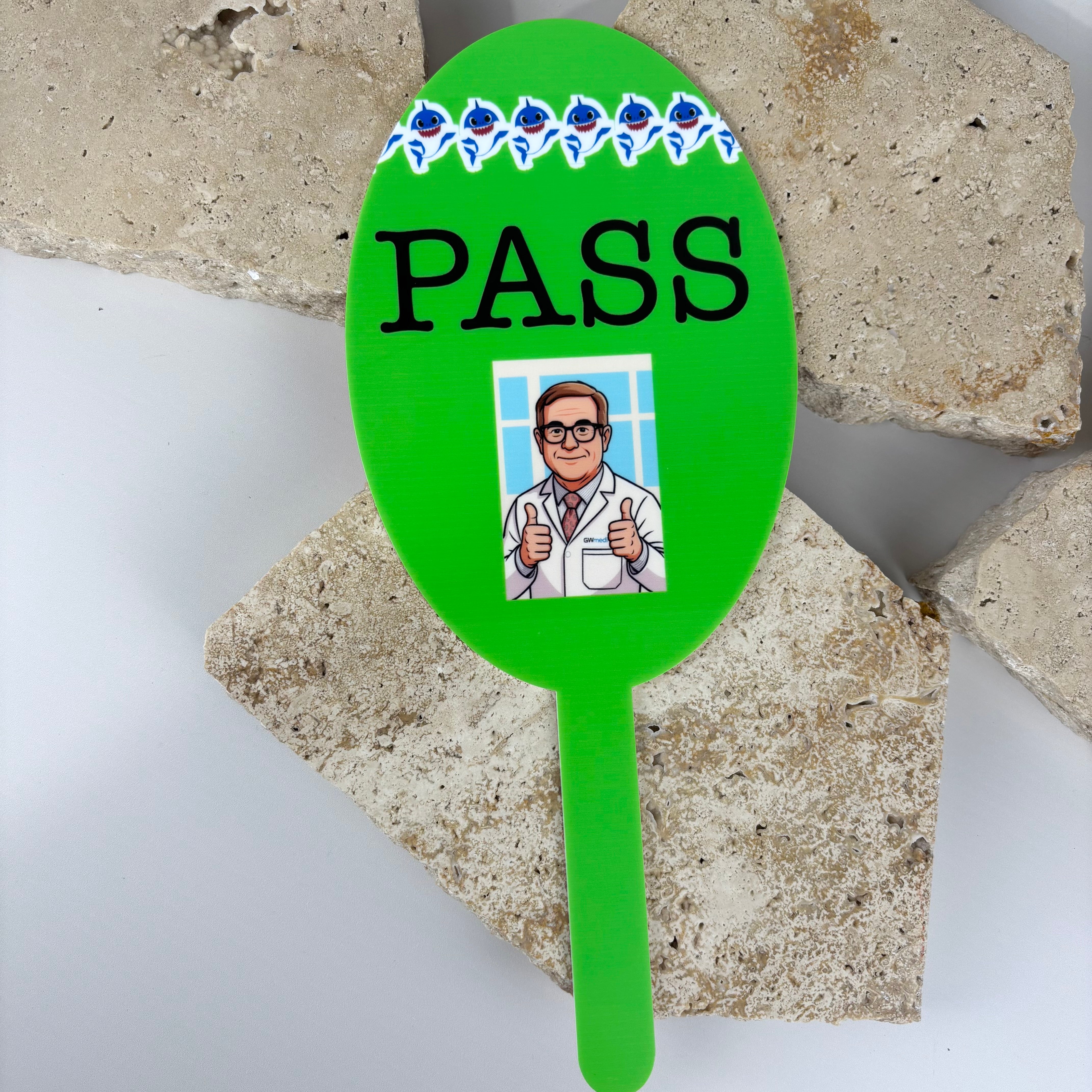 Green PASS paddle with cartoon doctor giving thumbs up, used for vision or eye test results