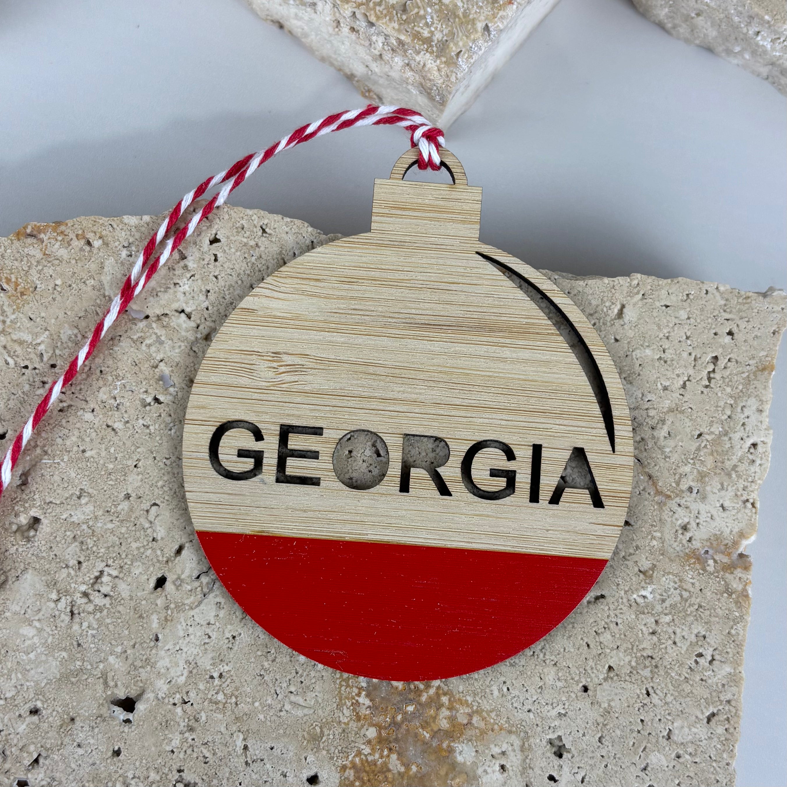 Personalised bamboo Christmas bauble ornament with name Georgia, featuring laser-cut lettering and a red painted base. Eco-friendly wooden design with red and white string, perfect for Christmas tree decorations or festive gifts.