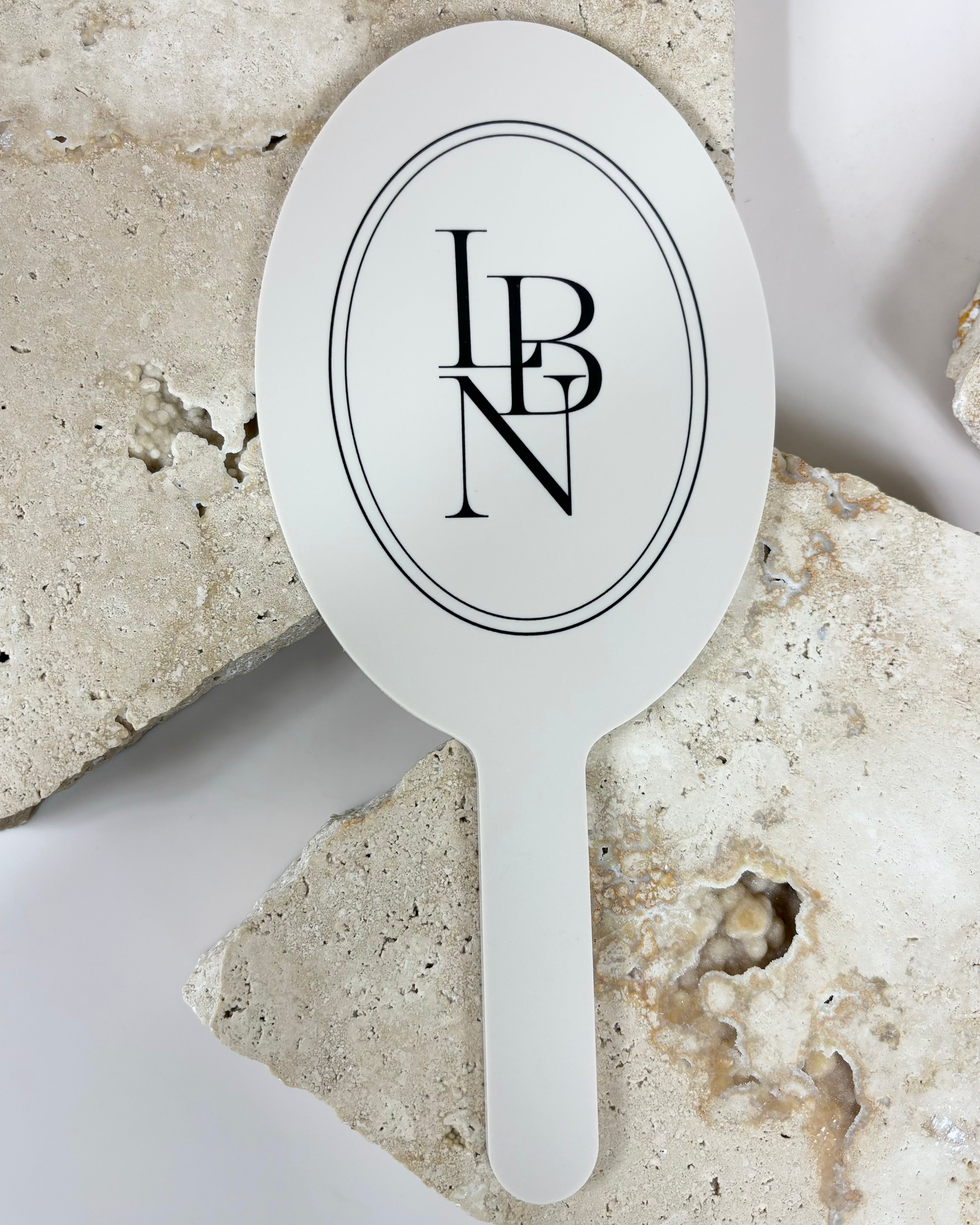 Custom oval handheld mirrors with LBN logo displayed on stone background