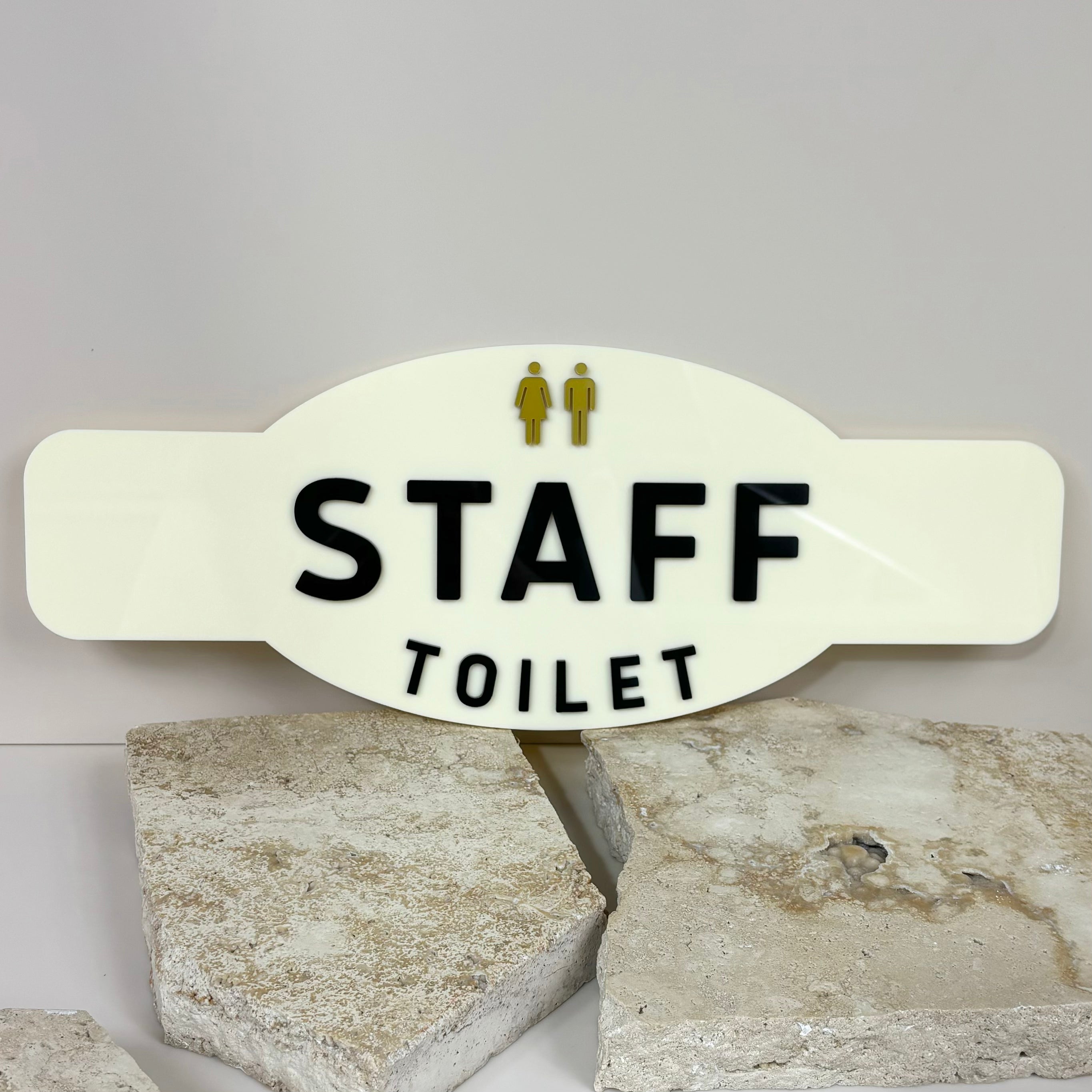 Staff toilet door plaque in cream acrylic with black text and universal icons, placed on stone background