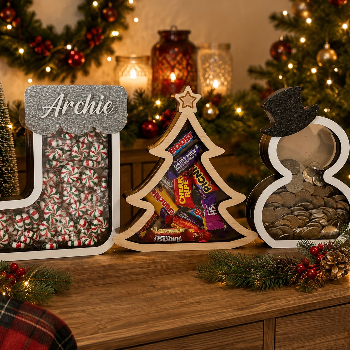 Personalised Christmas drop boxes in stocking, Christmas tree and snowman designs filled with lollies, chocolates and coins, displayed in a festive Christmas setting with personalised names.