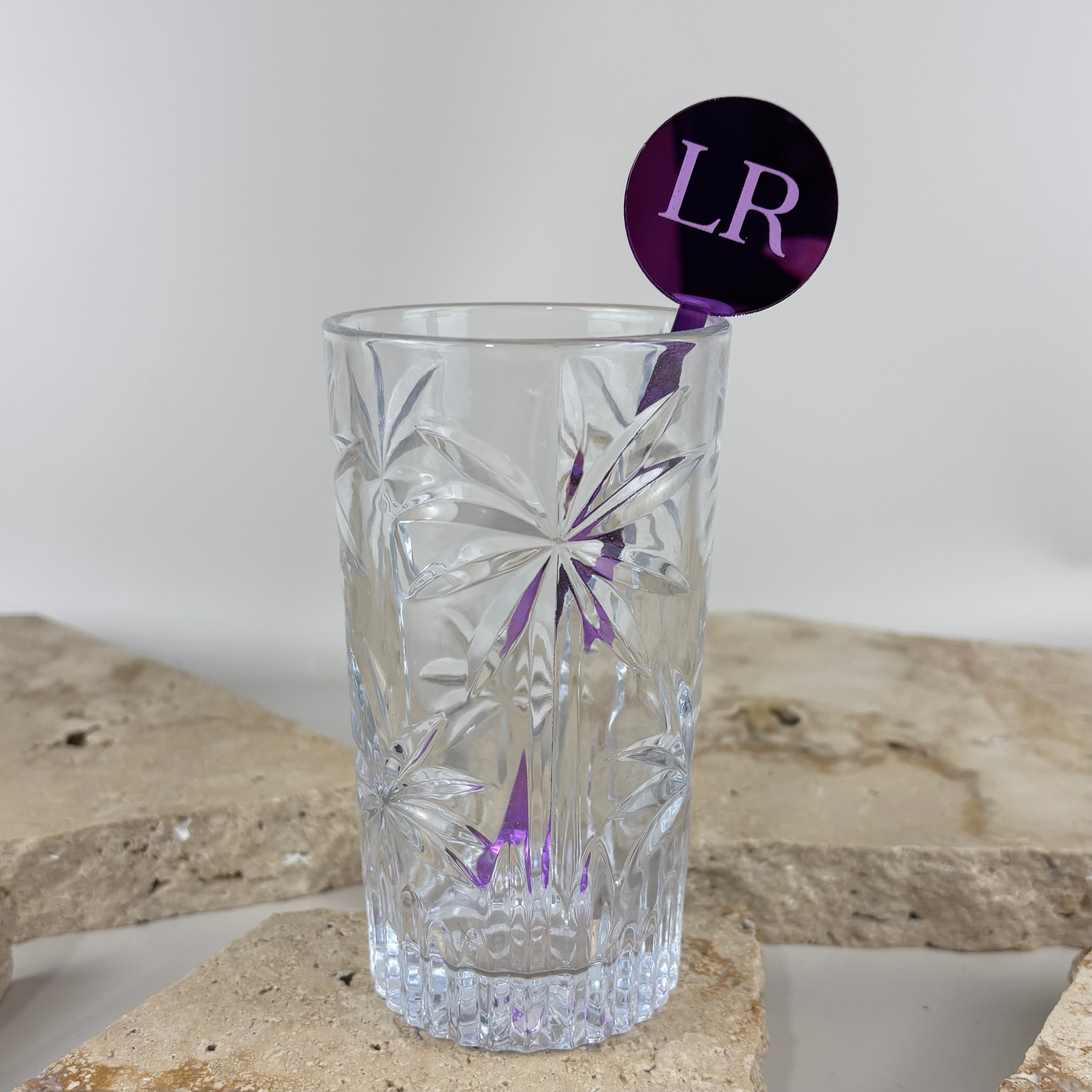 Clear cut glass tumbler with personalised purple acrylic drink stirrer featuring LR initials, custom bar accessory for events and celebrations