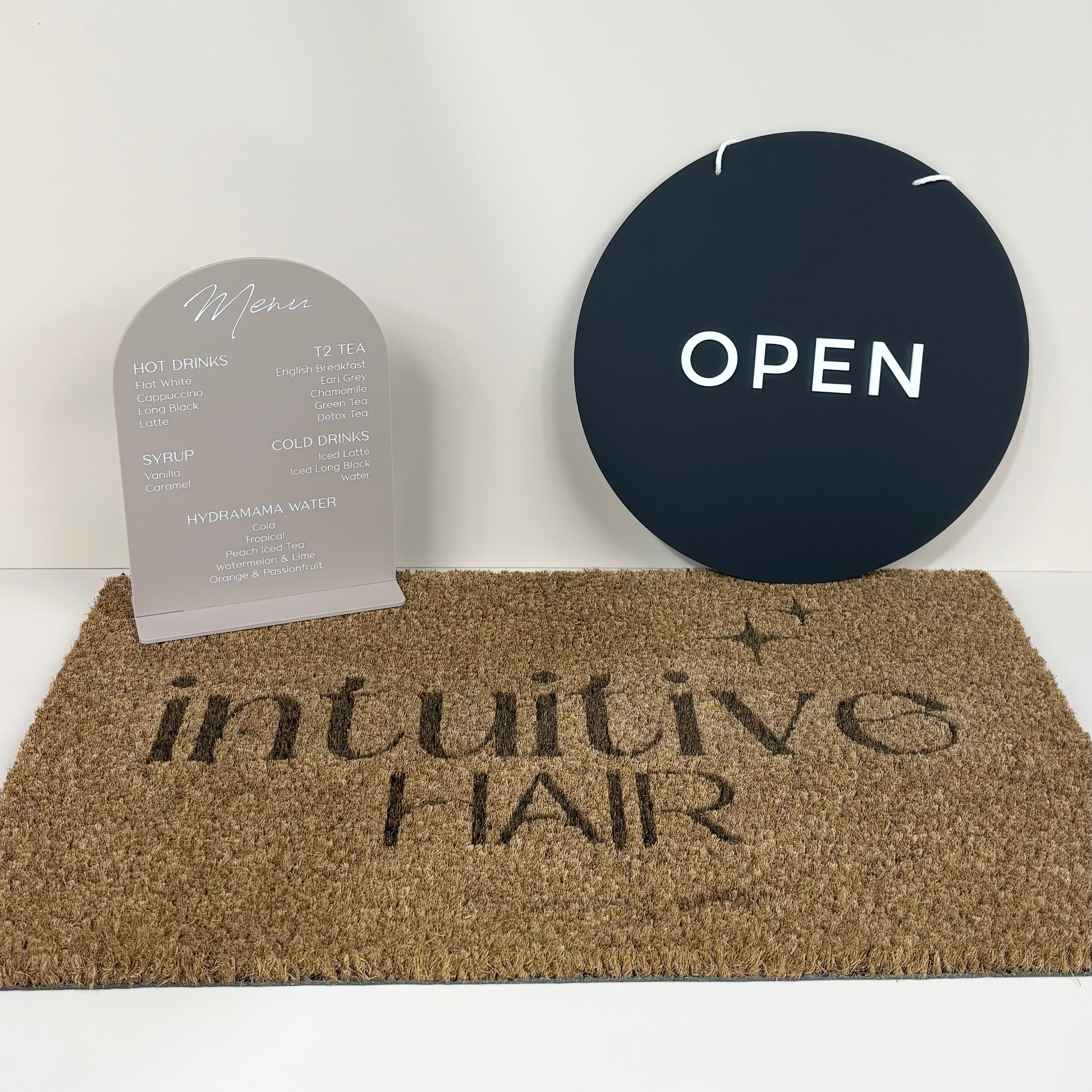 Dark round acrylic ‘Open’ sign and grey arch sign on cork mat for Intuitive Hair salon
