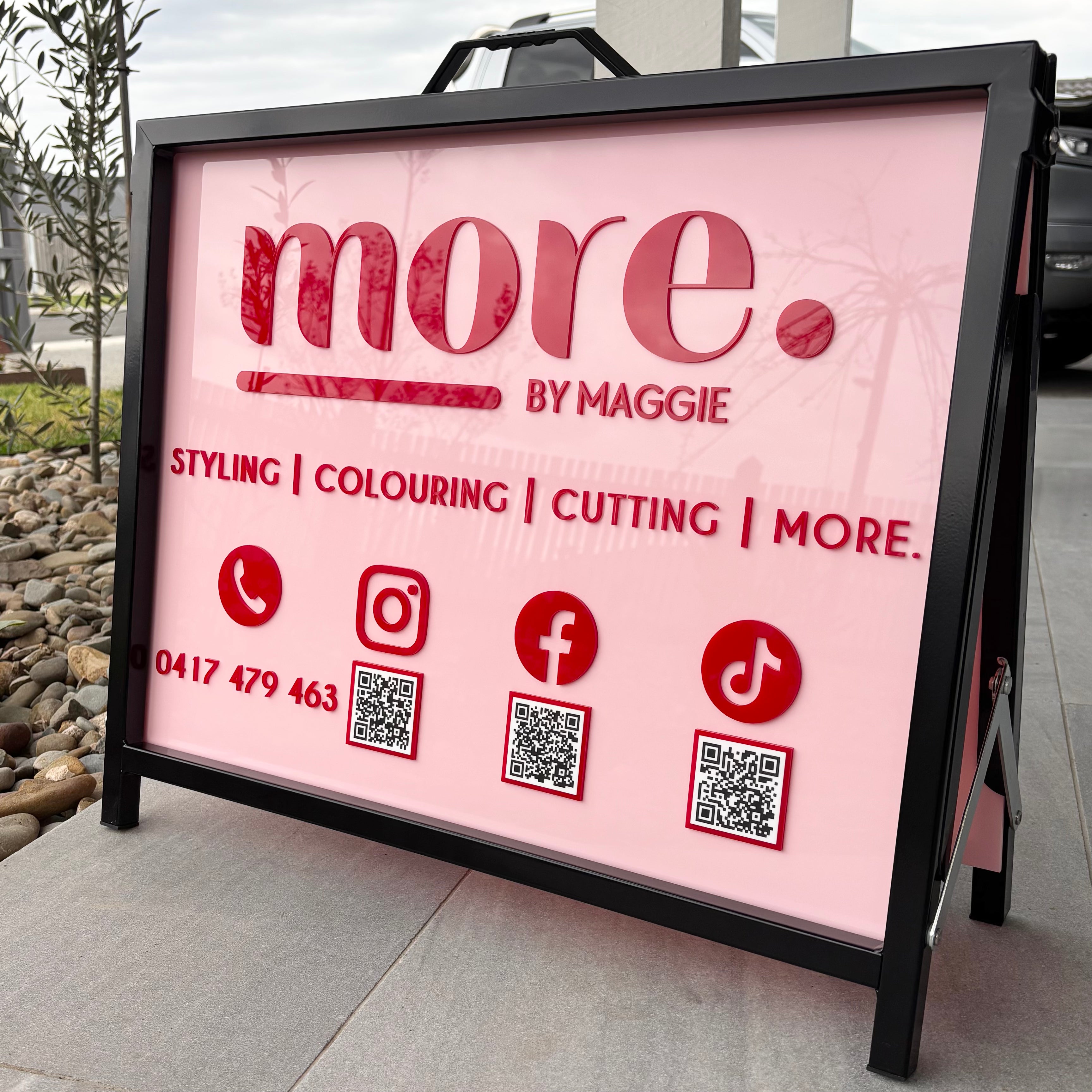Custom pink and red acrylic A-frame salon sign for More by Maggie featuring 3D lettering, styling and colouring services, phone number, Instagram, Facebook and TikTok icons with QR codes for easy booking and social media connection